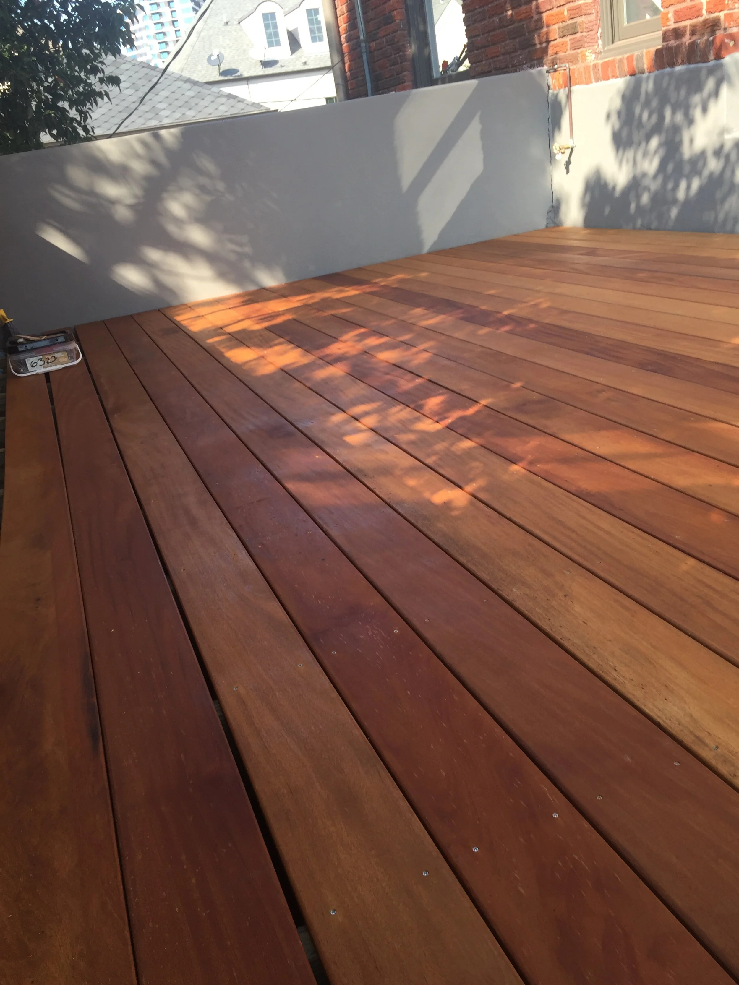 Freshly installed wooden deck with sunlight and shadows, surrounded by a brick and plaster wall.