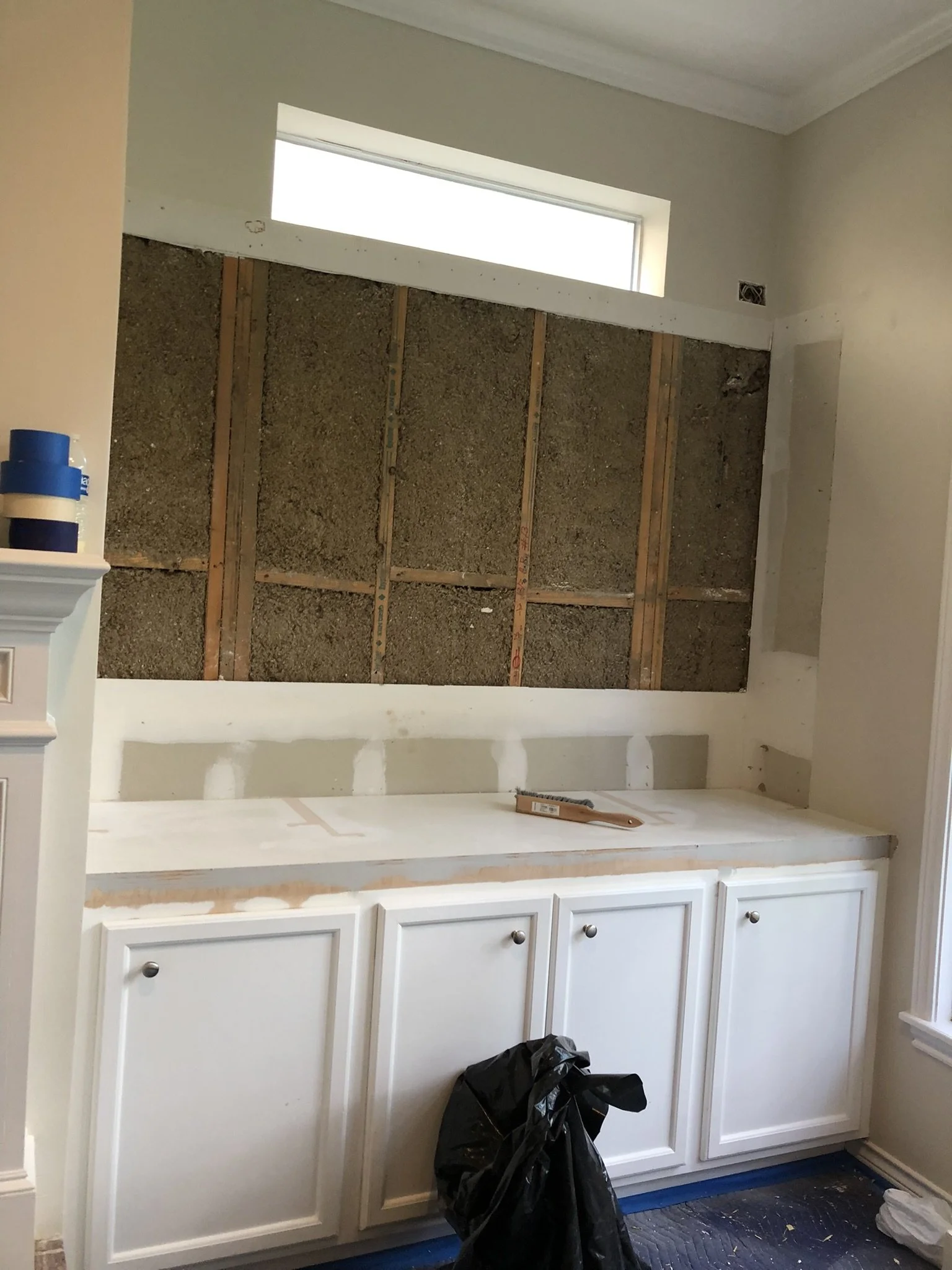 Kitchen renovation in progress, featuring partially finished white cabinets and a bare wall with exposed framework.