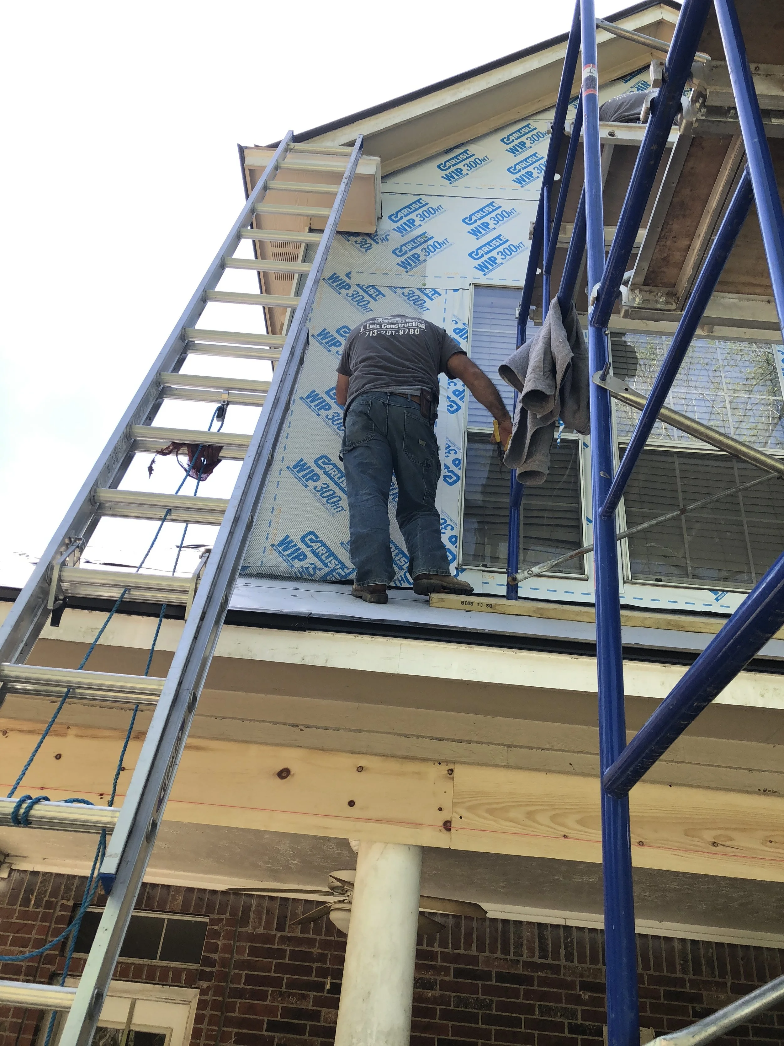 Construction worker on ladder and scaffold installing house siding
