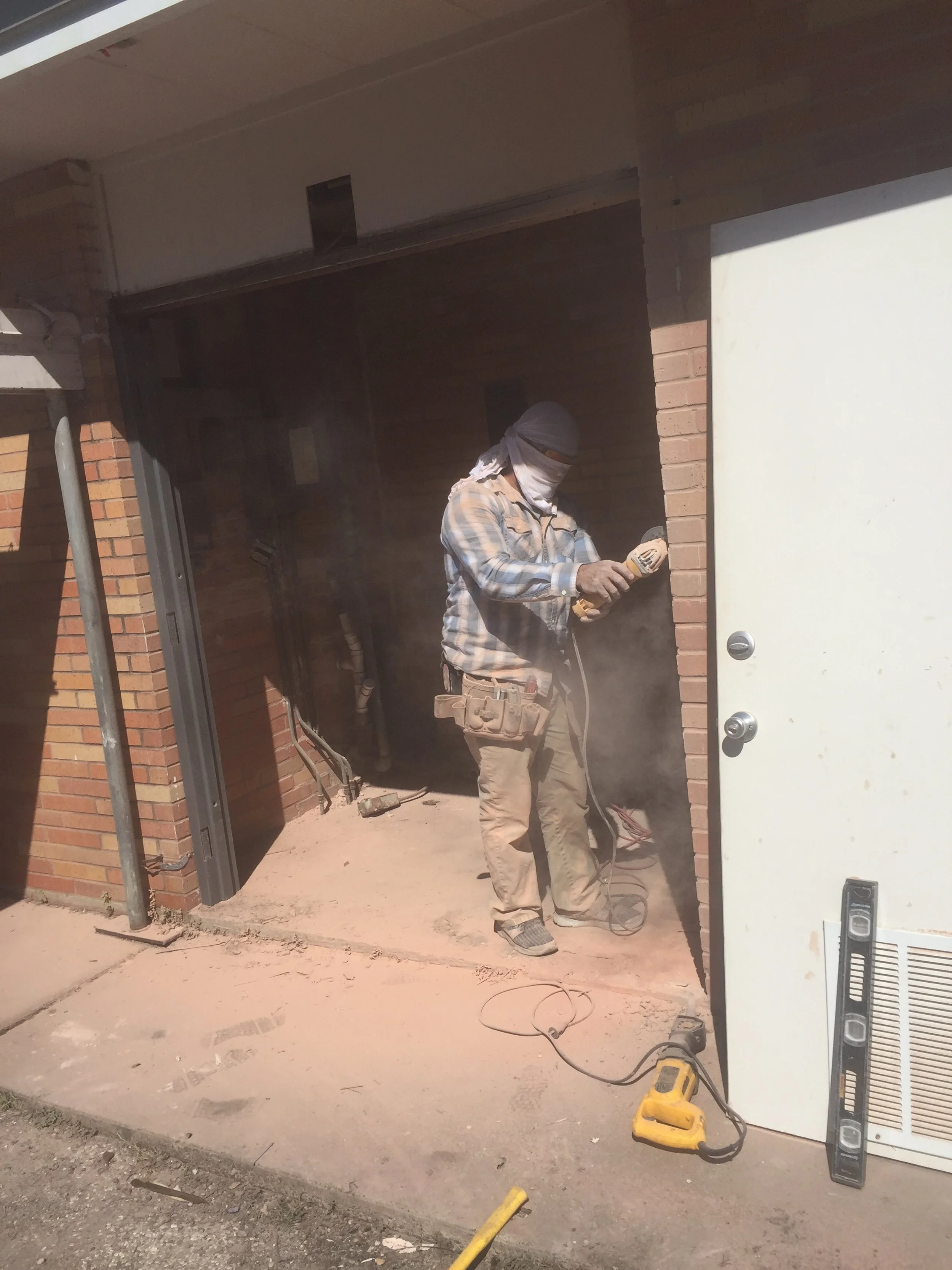 Person cutting brick wall with power tool, wearing protective gear
