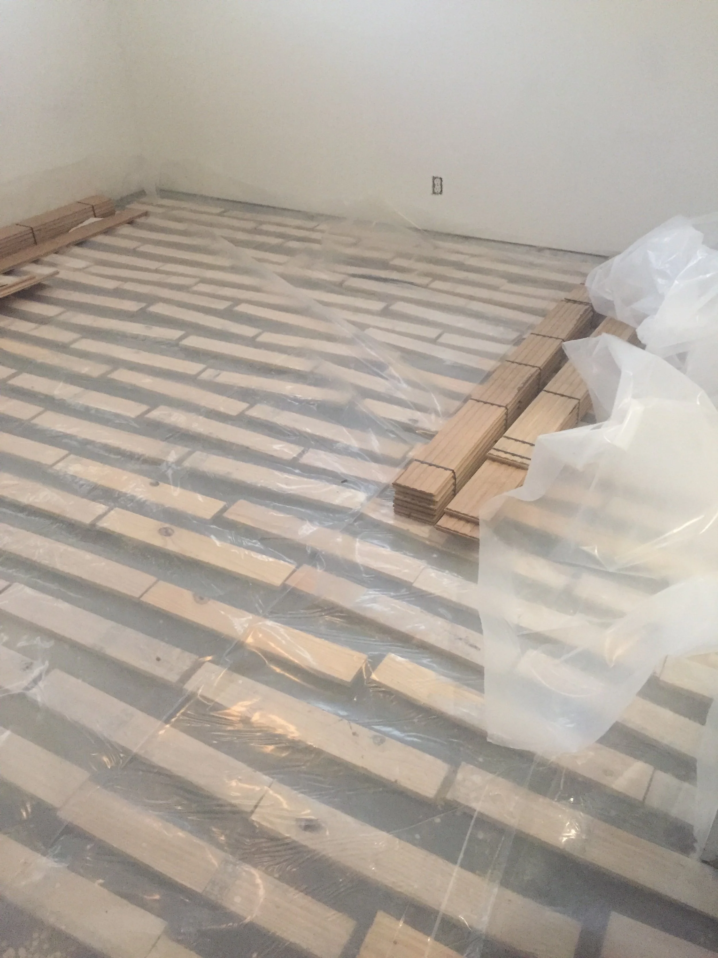 Room under flooring installation with wooden planks and plastic sheeting
