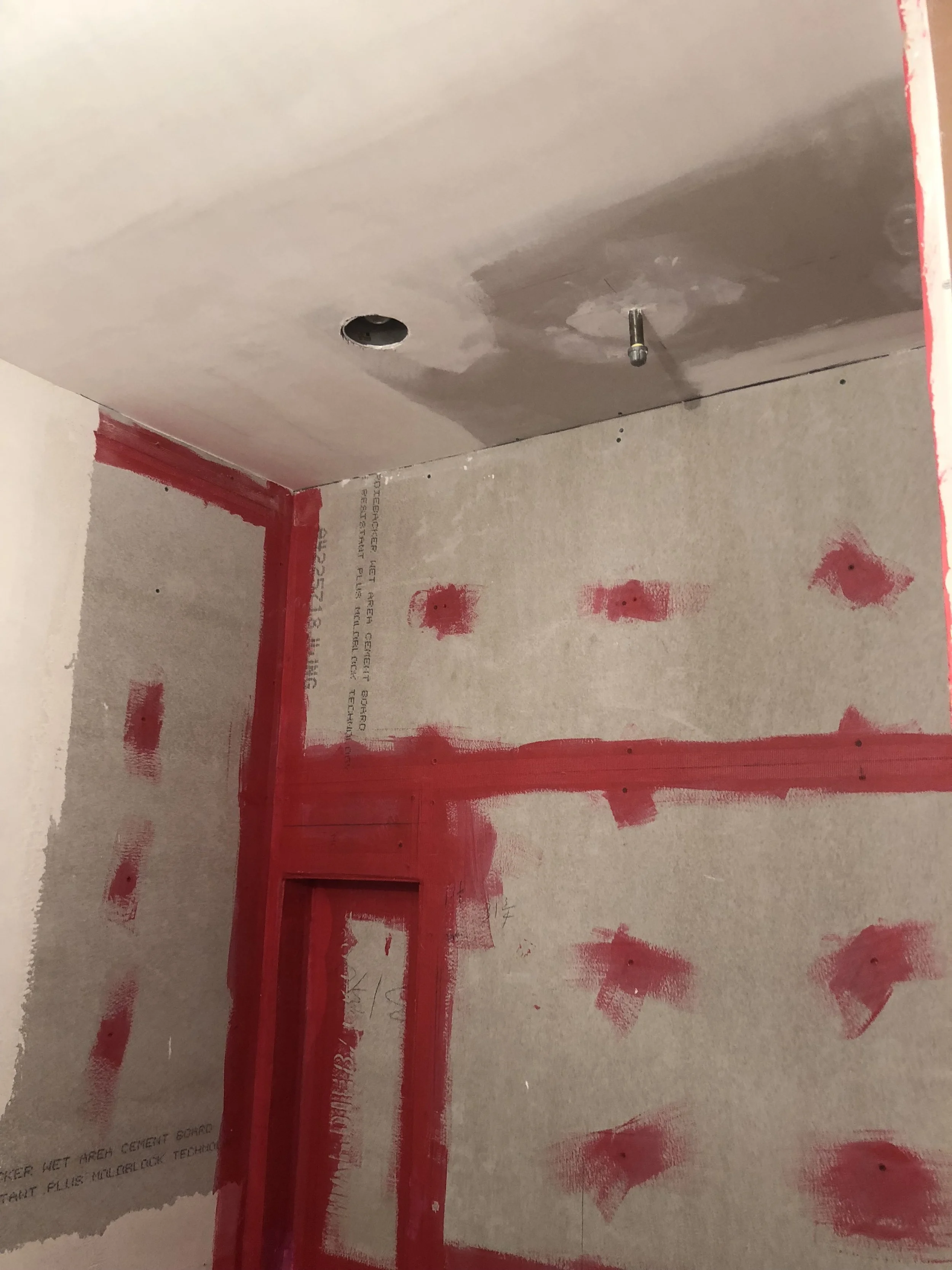 Bathroom under construction with cement board walls and red waterproofing tape and sealant applied at seams and screw holes.