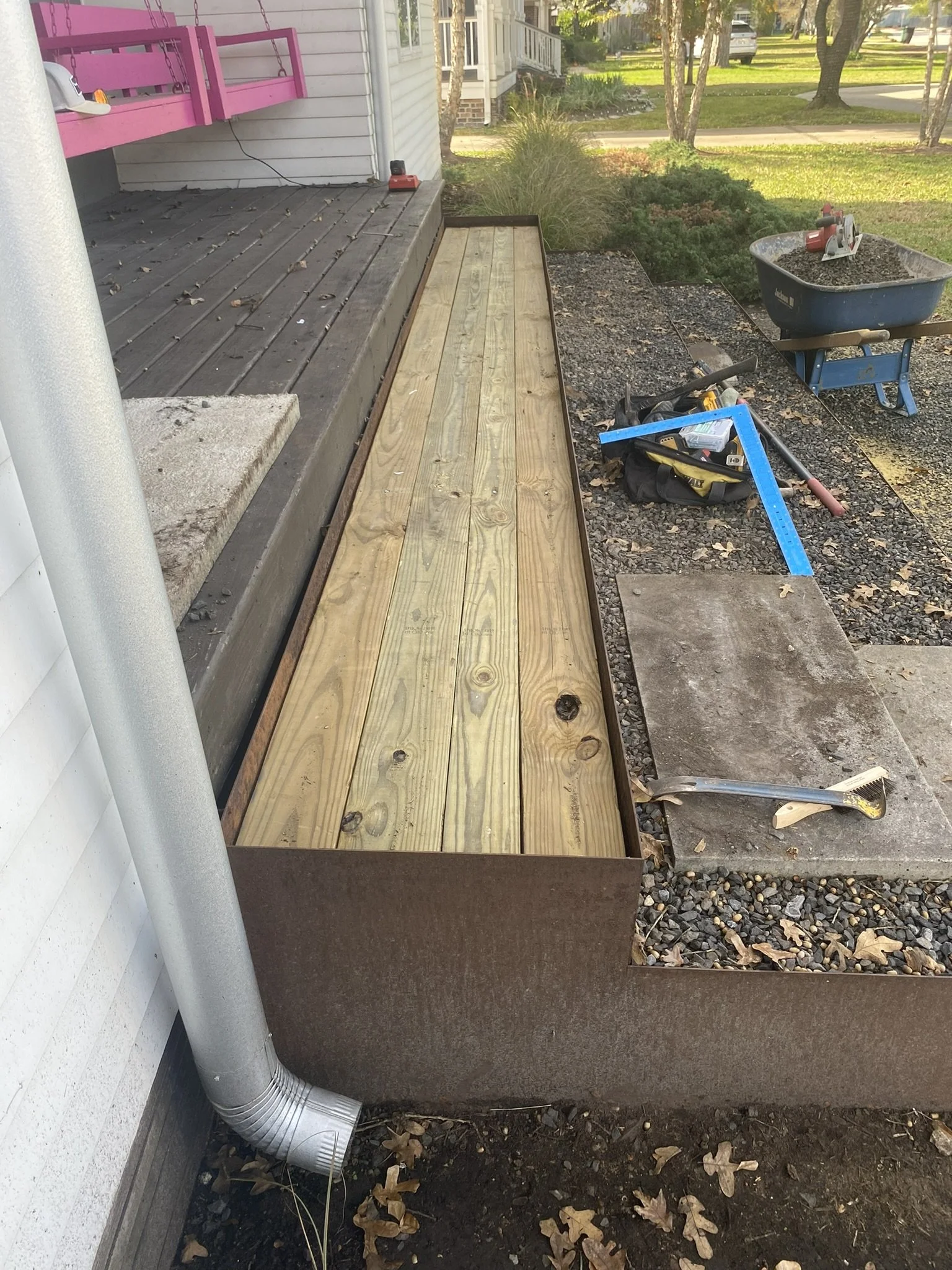 Wooden ramp under construction on a porch with tools and a wheelbarrow nearby.