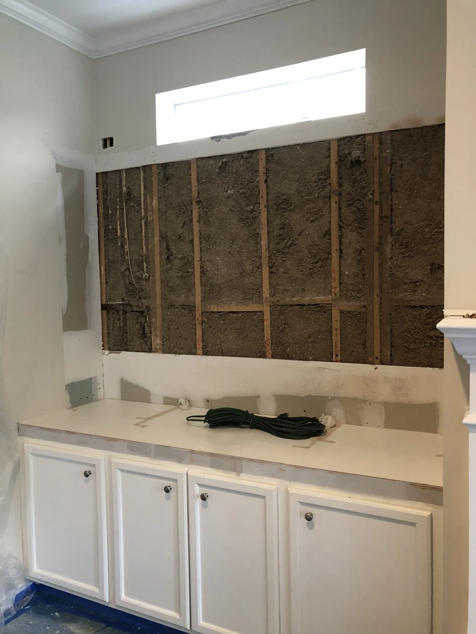 Kitchen under renovation with exposed wall, white cabinets, and coiled green wire on countertop.