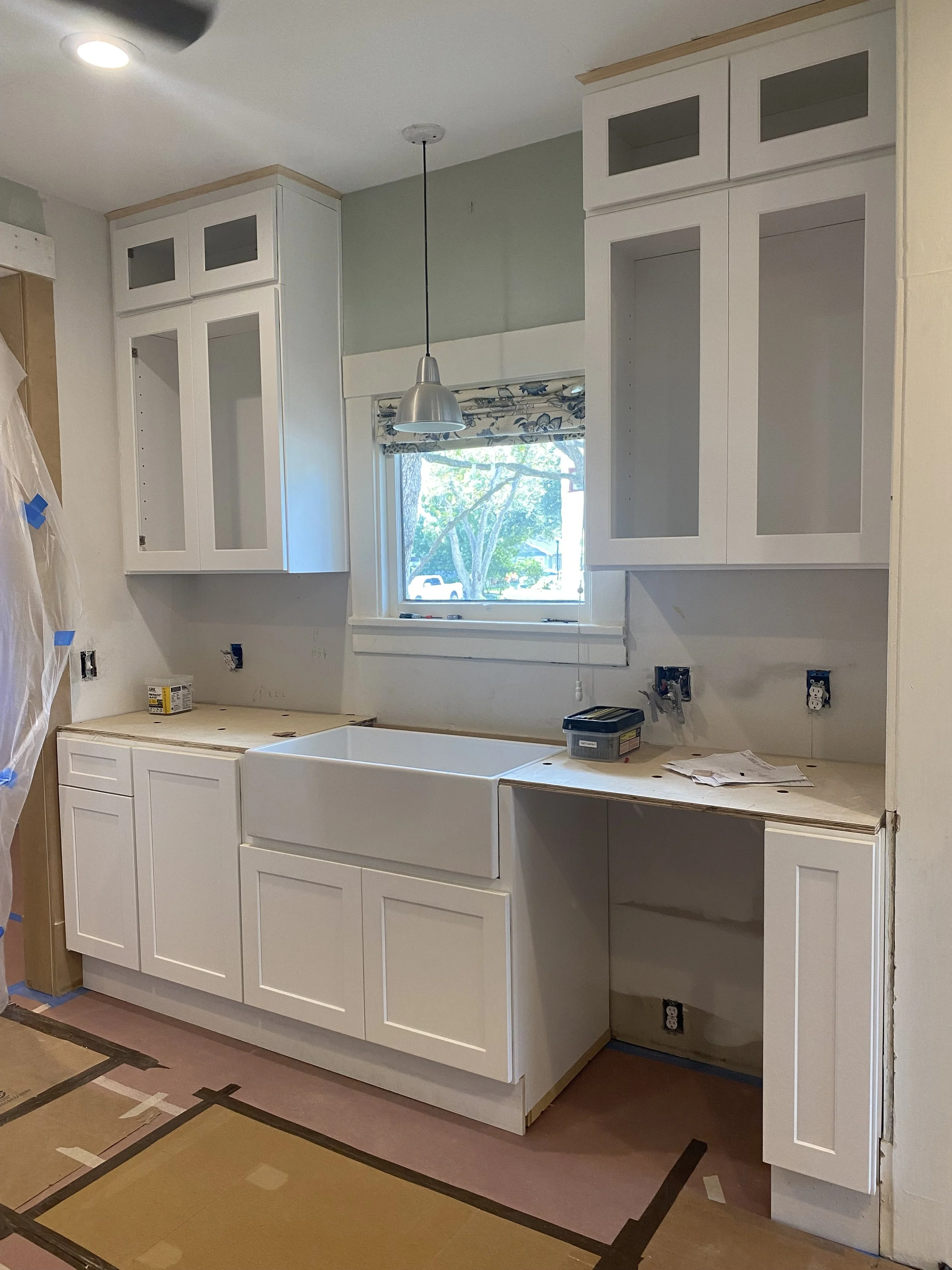 Kitchen under renovation with white cabinets, farmhouse sink, and pendant light.