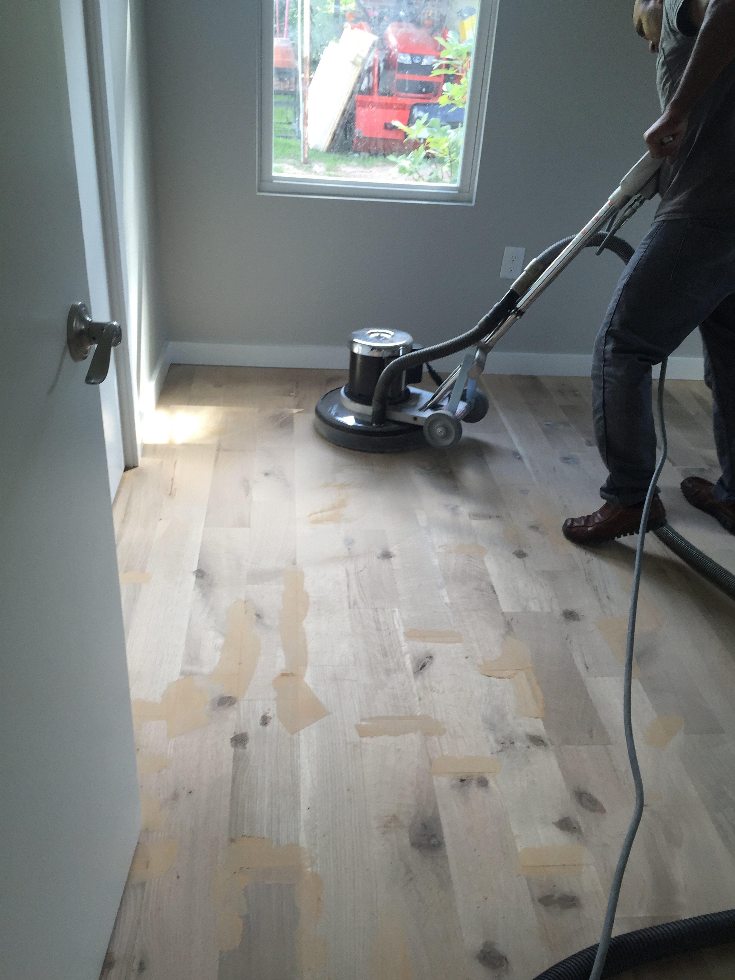 Person using a floor sander on a wooden floor indoors