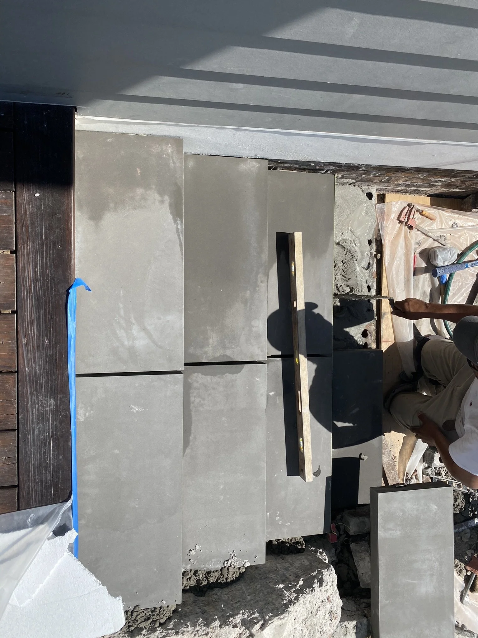 Large gray tiles being installed on steps outdoors with construction materials and tools visible.