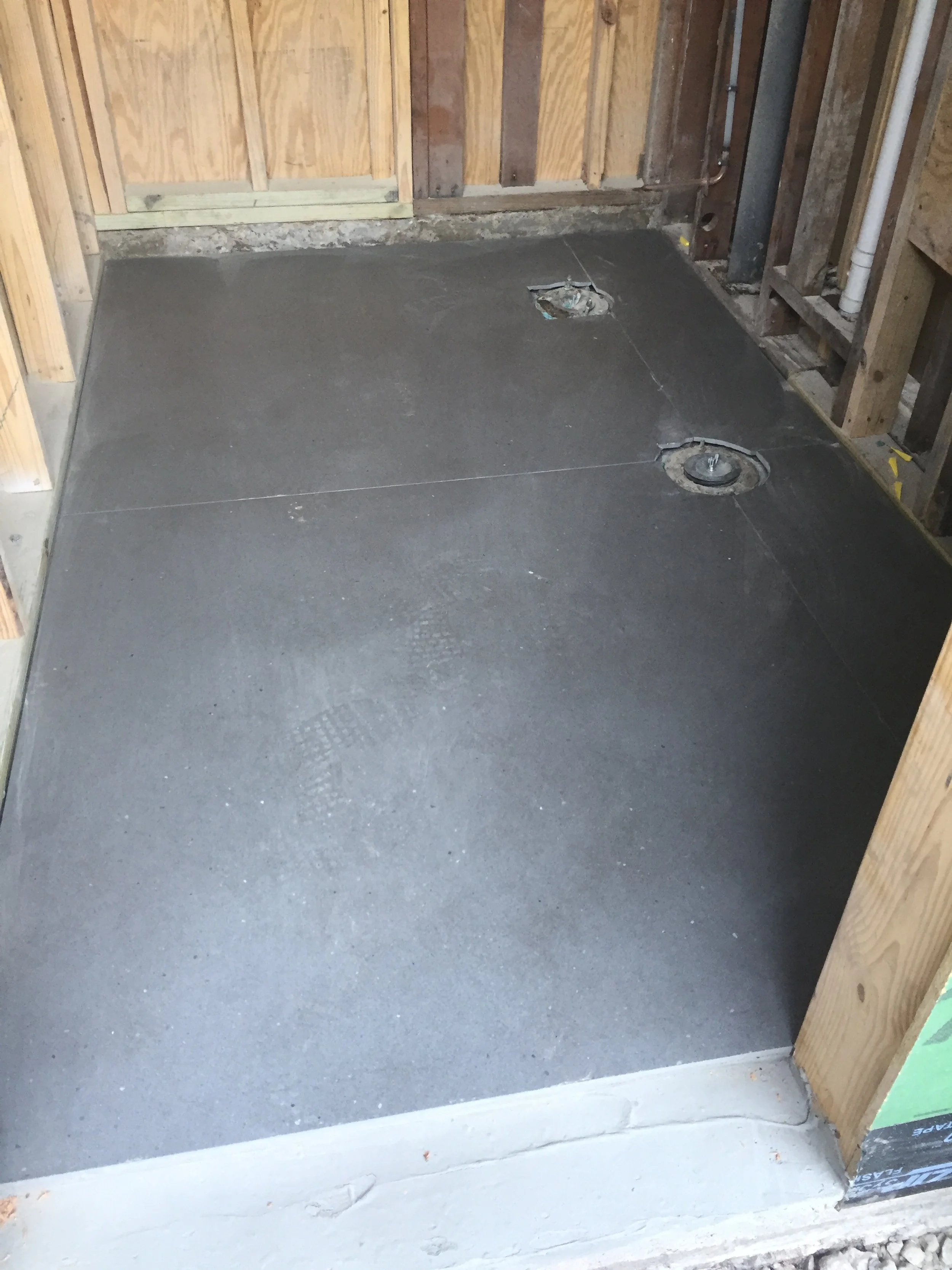 Concrete floor with two circular drain openings inside a partially constructed wooden room.