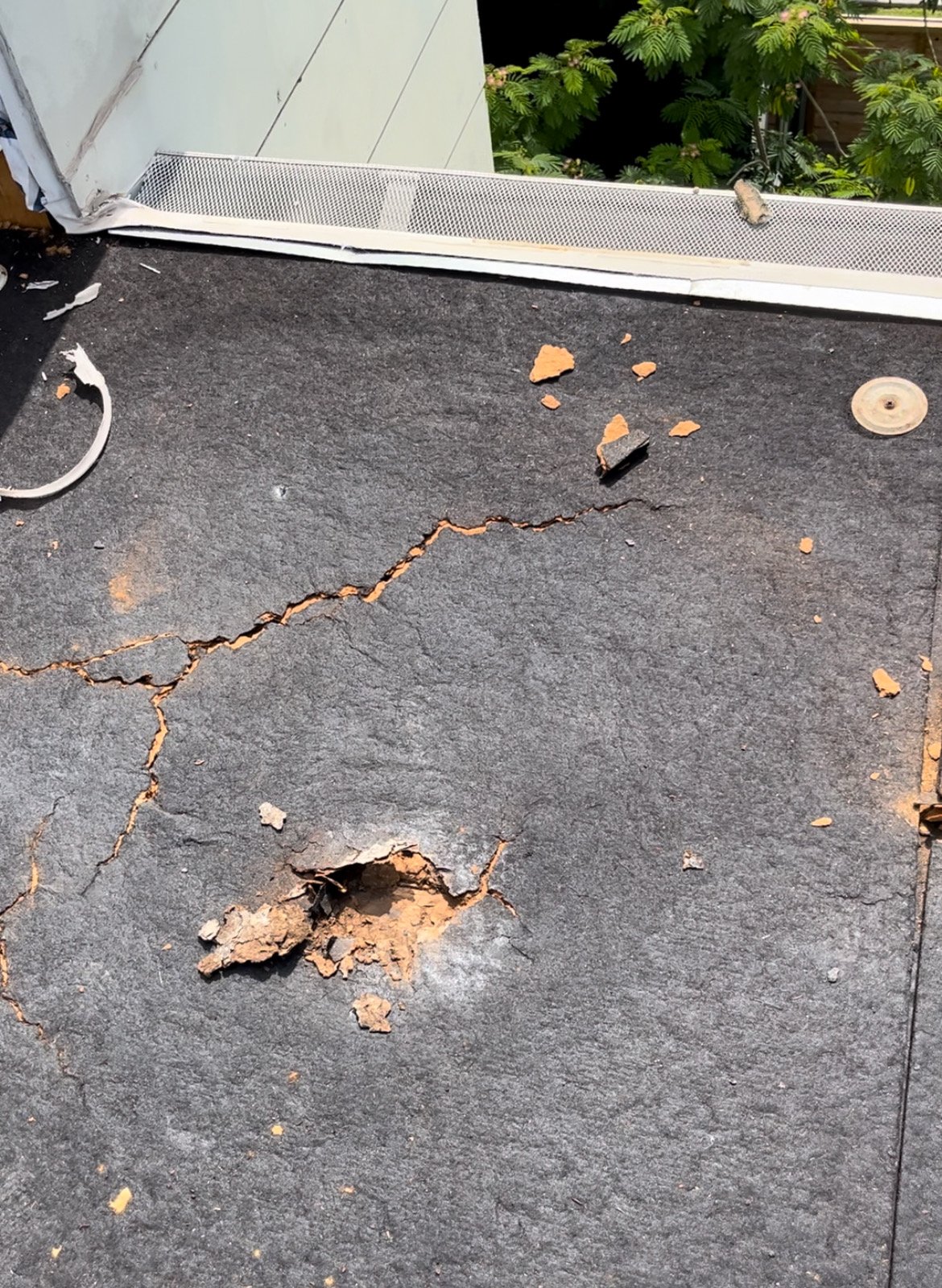 Damaged roof with crack and hole in black roofing material