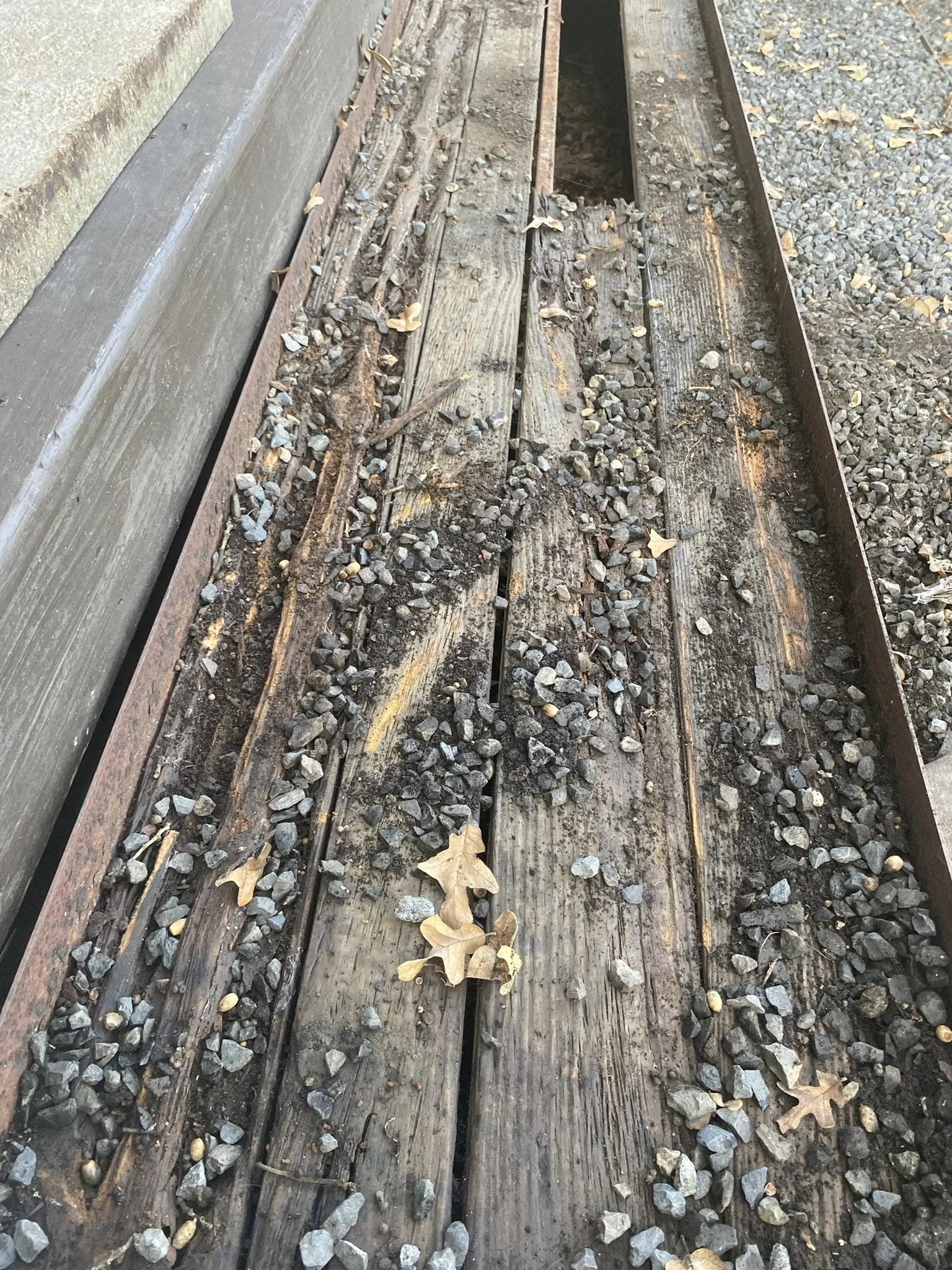 Close-up of an old wooden railway track with scattered gravel and dried leaves.