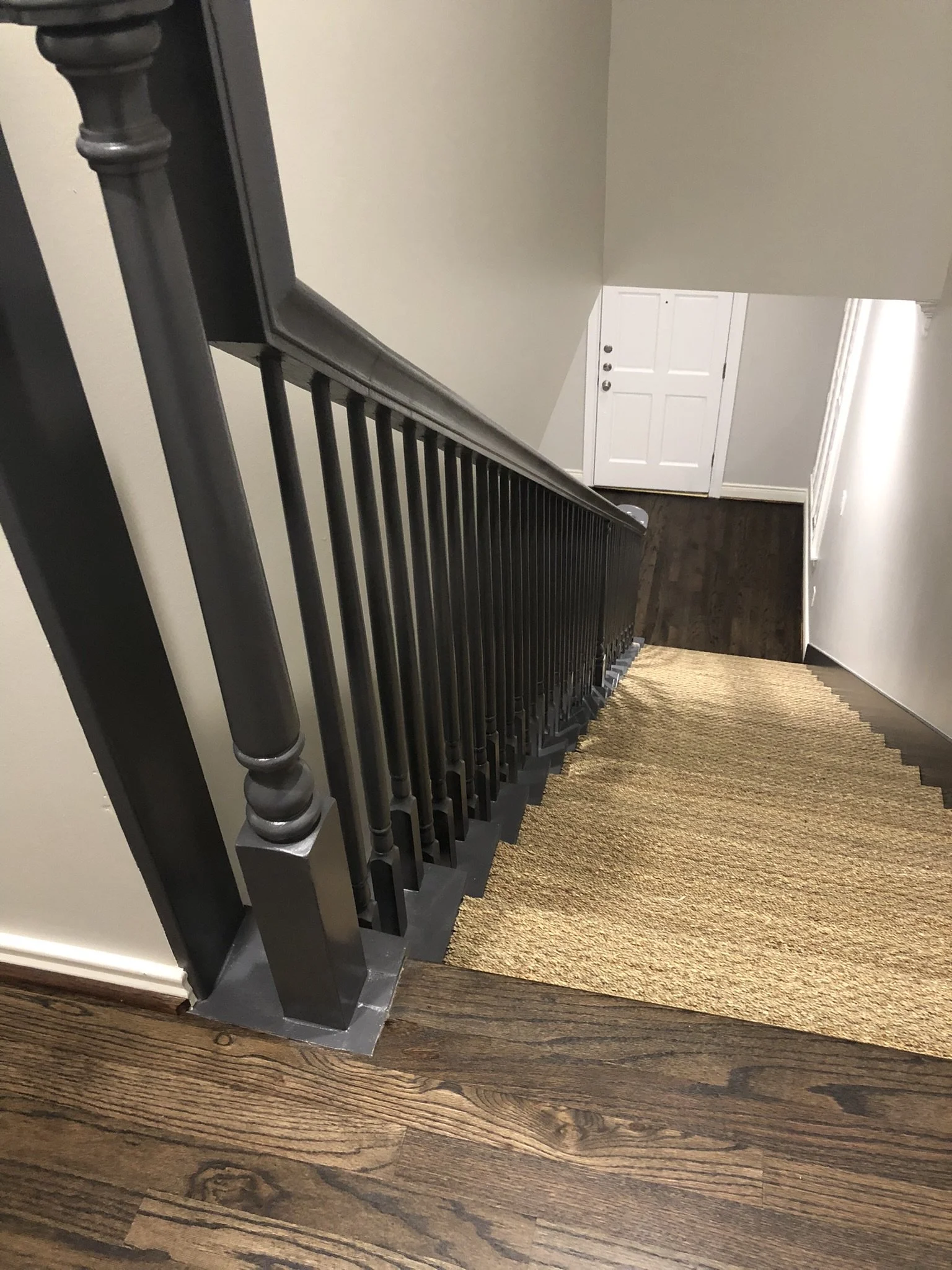 Wooden staircase with dark metal balustrade, leading down to a white door at the bottom, carpet overlay on steps.