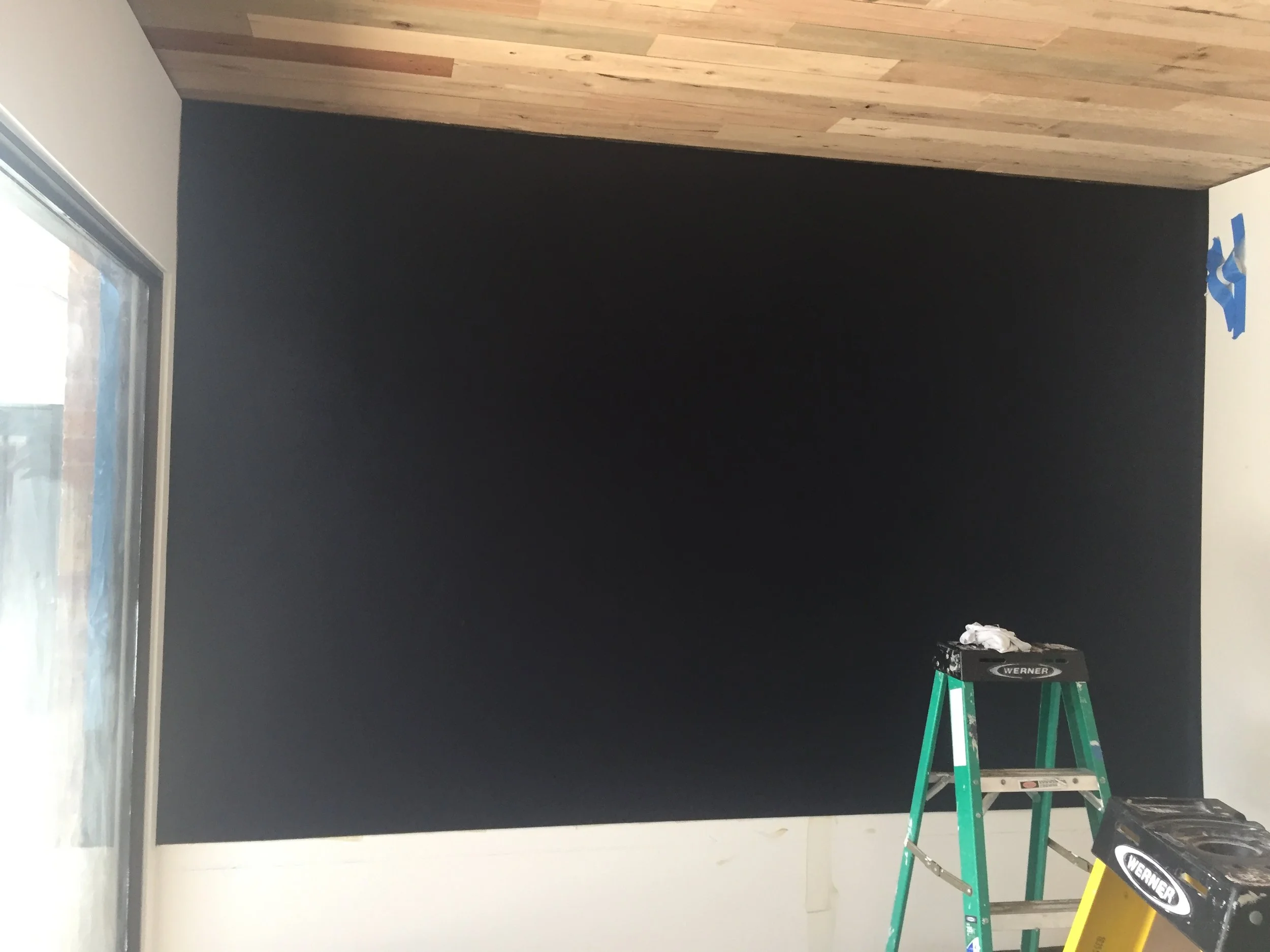 Room with black painted wall, wood ceiling, and a green ladder.