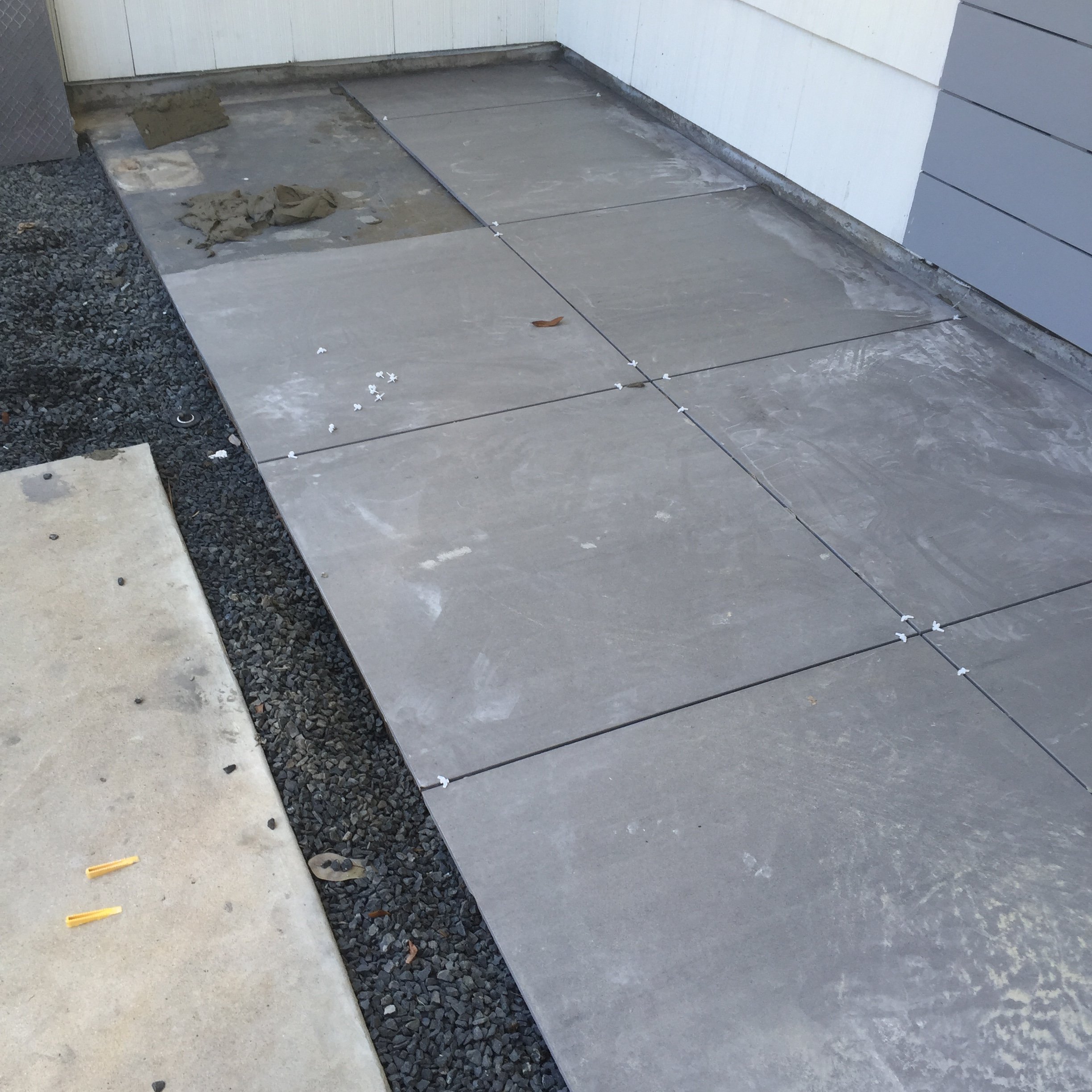 Partially installed gray floor tiles with grout and spacers on a concrete surface.