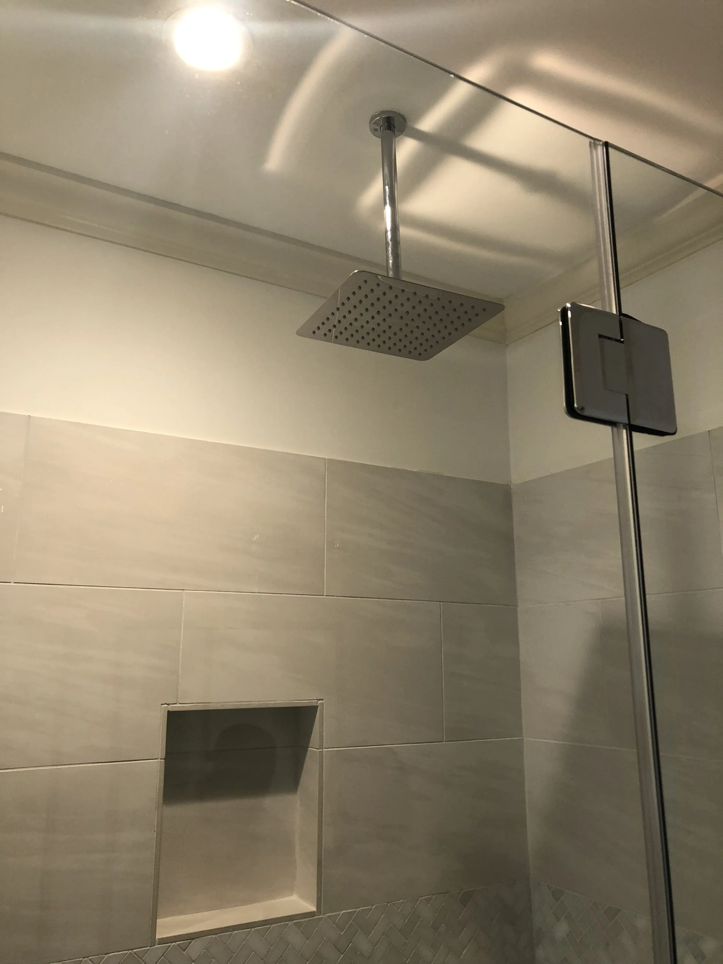 Modern bathroom shower with large square showerhead, recessed shelf, tiled wall, and frameless glass door.