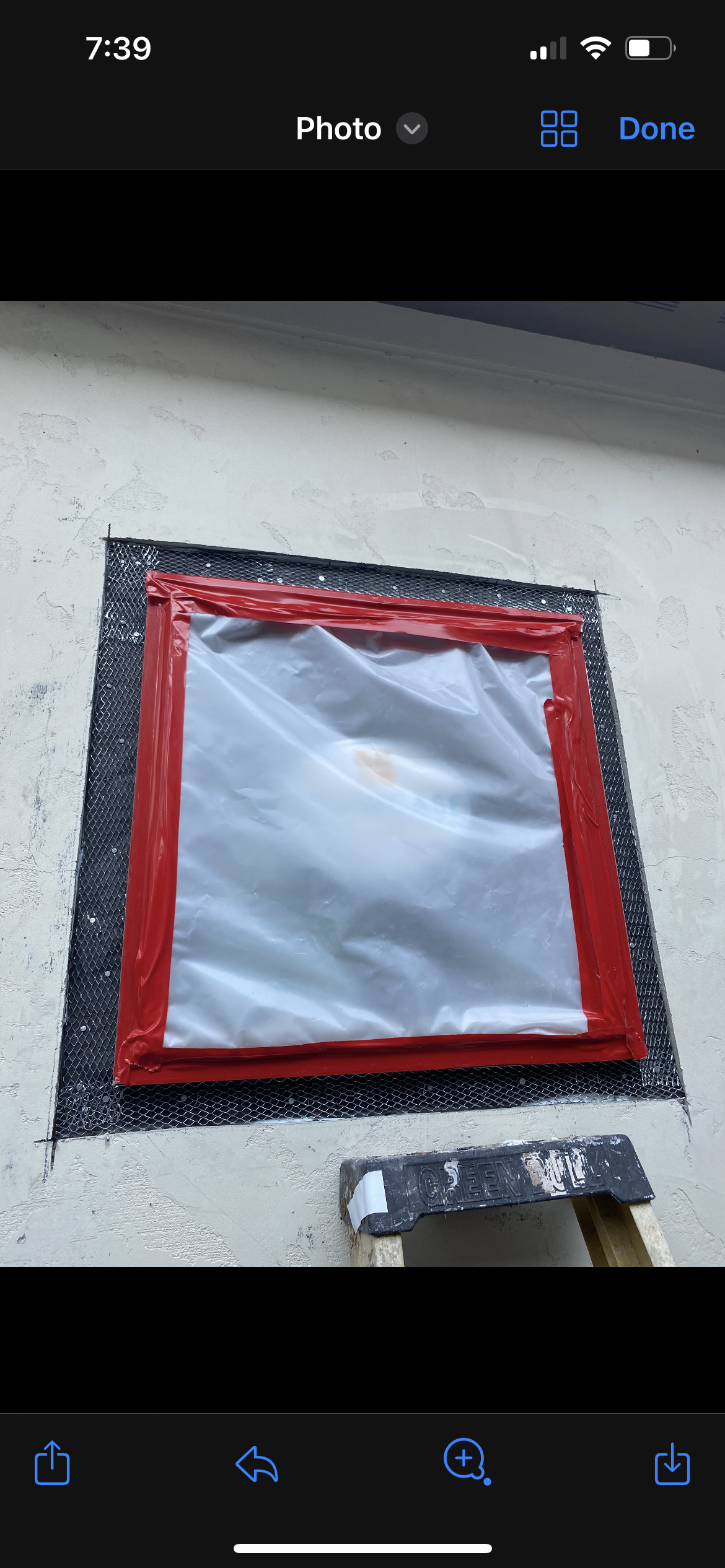 Window covered with plastic sheeting and red tape on stucco wall with ladder nearby.