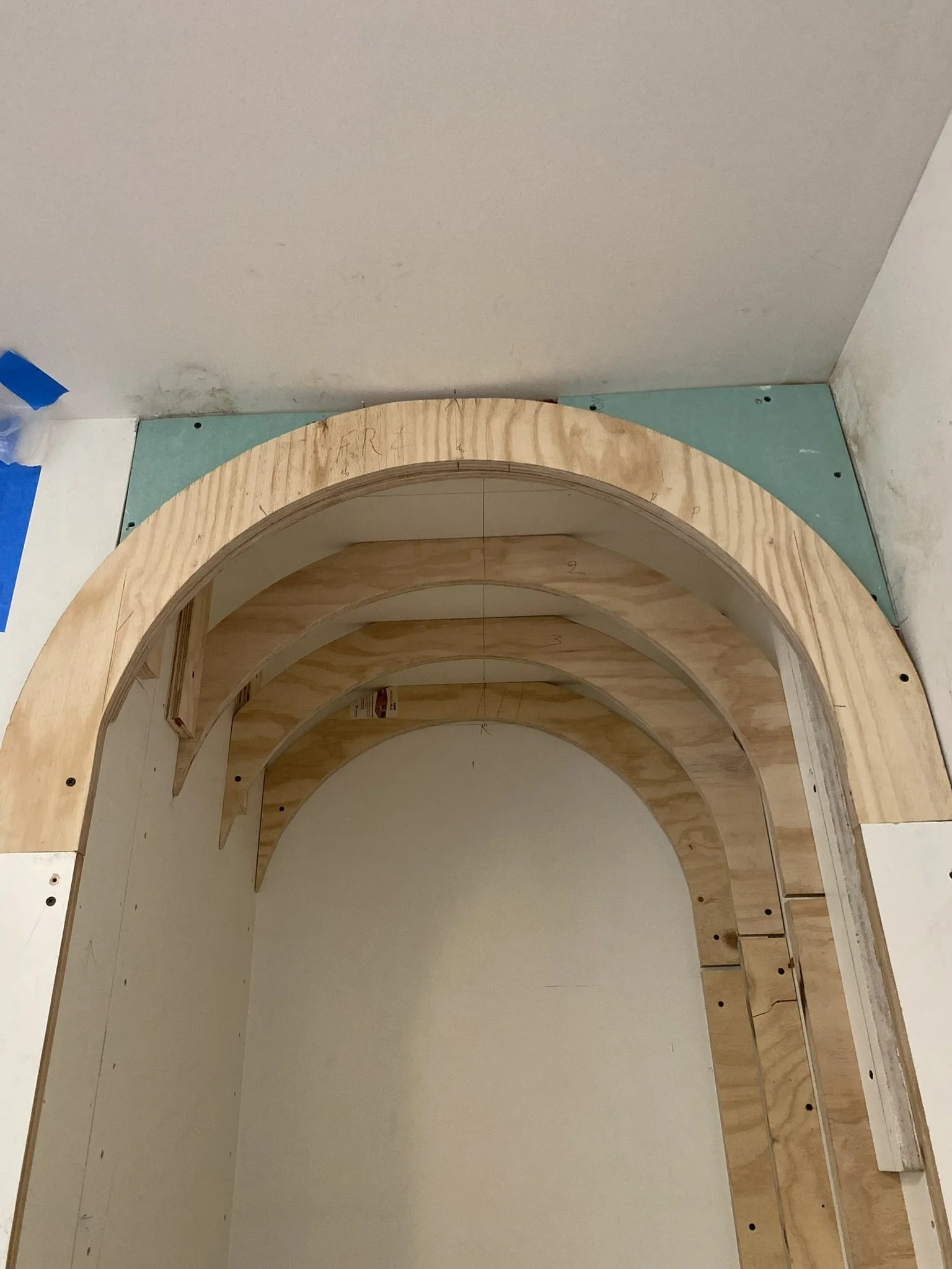 Wooden archway under construction with plywood framing against a wall.