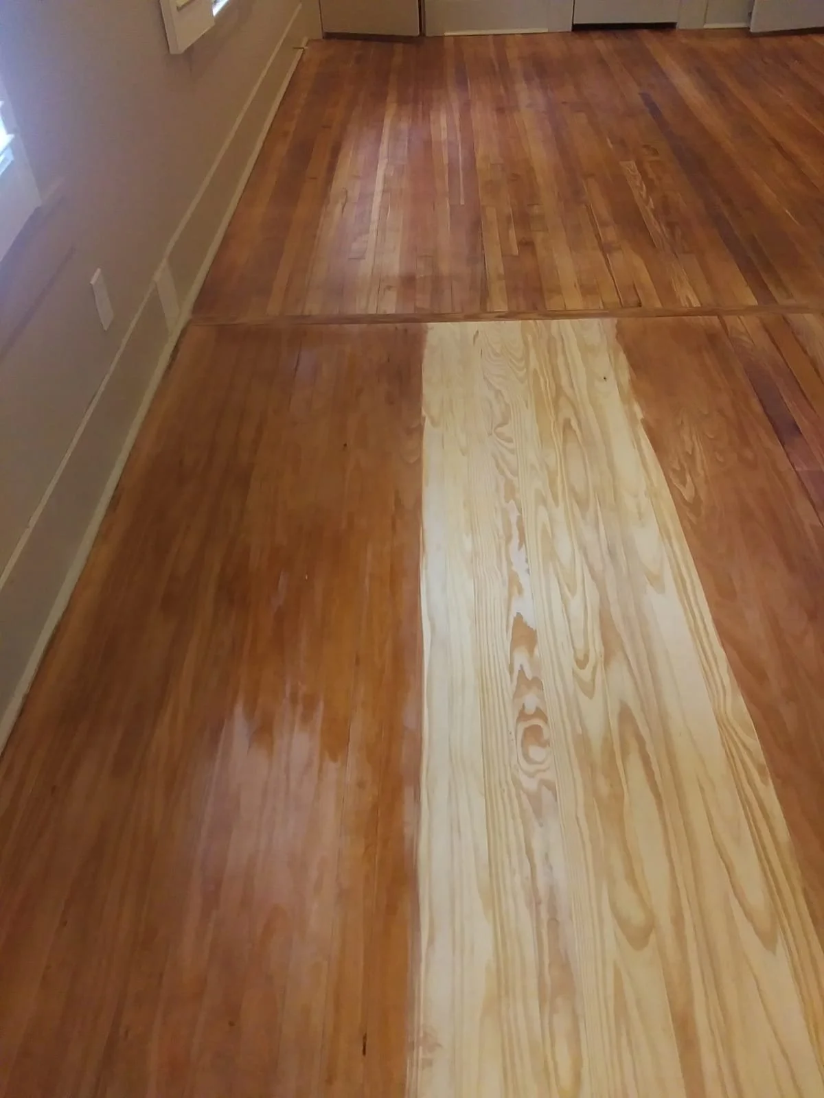 Wood floor with different stages of refinishing, showing unfinished and finished areas, with visible color and texture contrast.