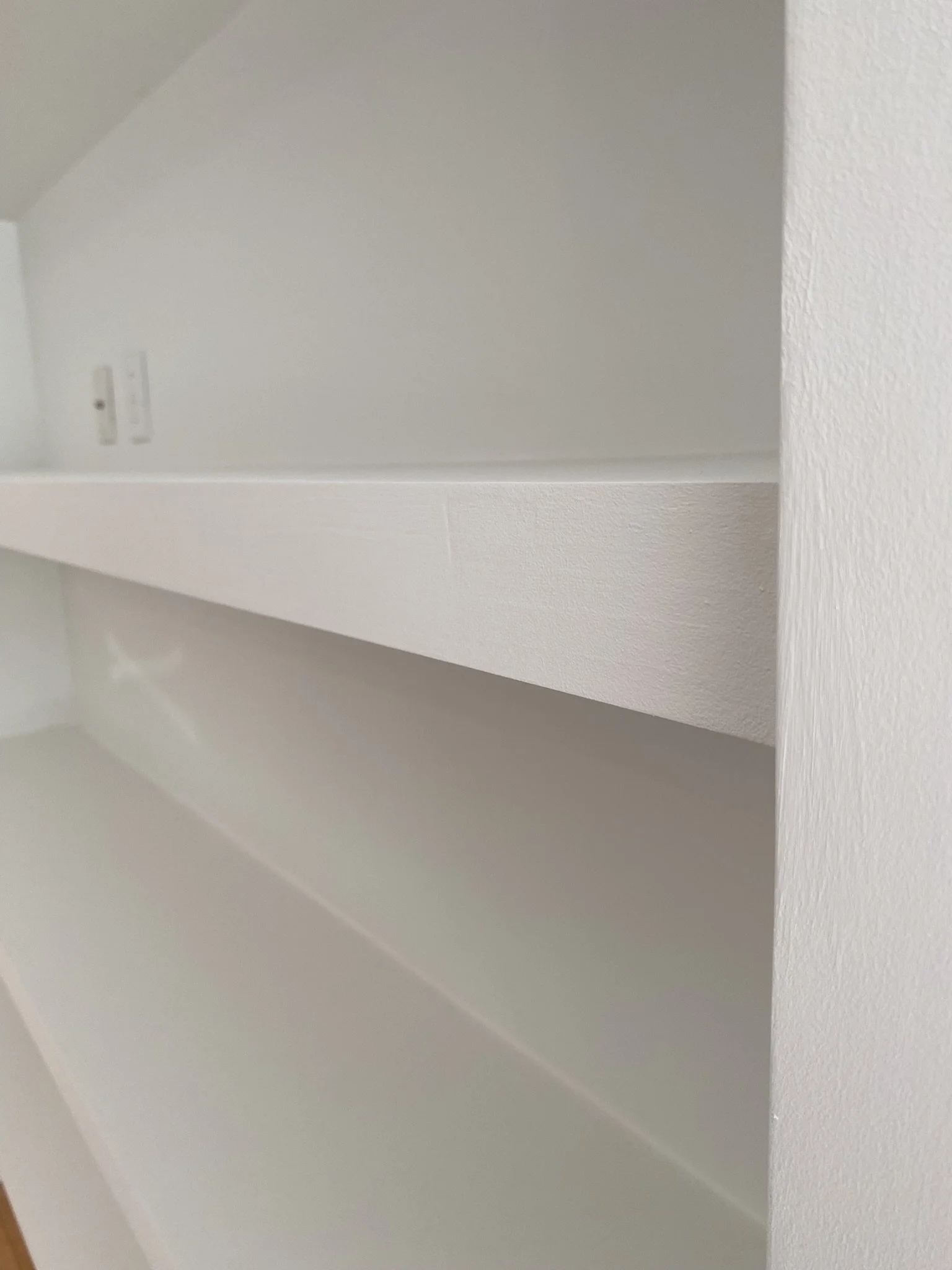 White painted built-in shelves with two electrical outlets on the wall.