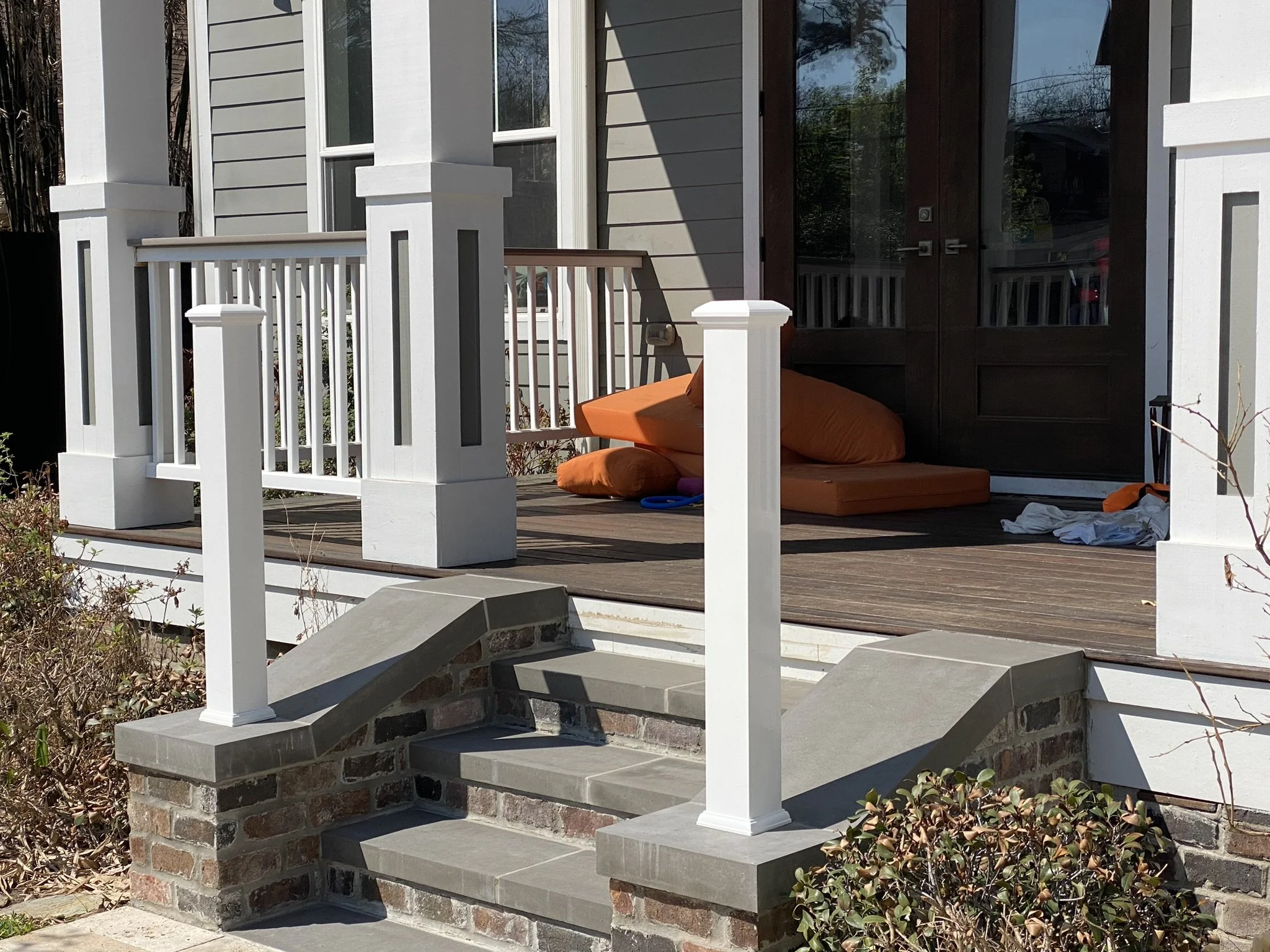 Front porch with white columns, brick steps, and a dark wooden door; orange cushions and a towel are on the porch floor.