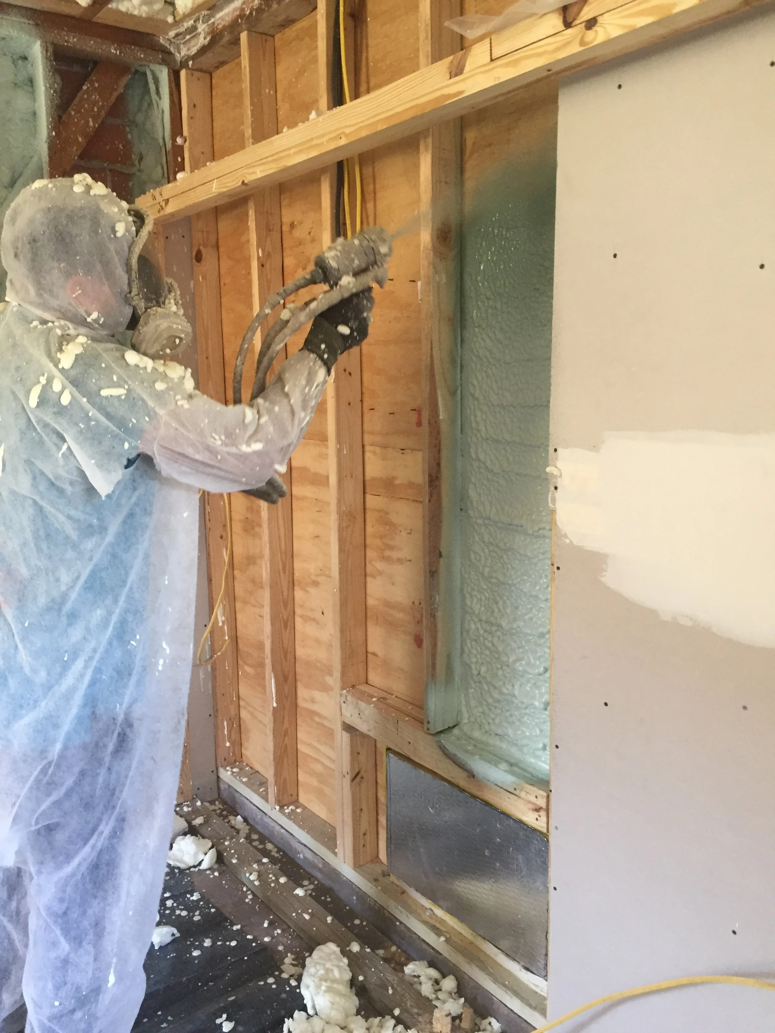 Person in protective gear spraying foam insulation on a wall.