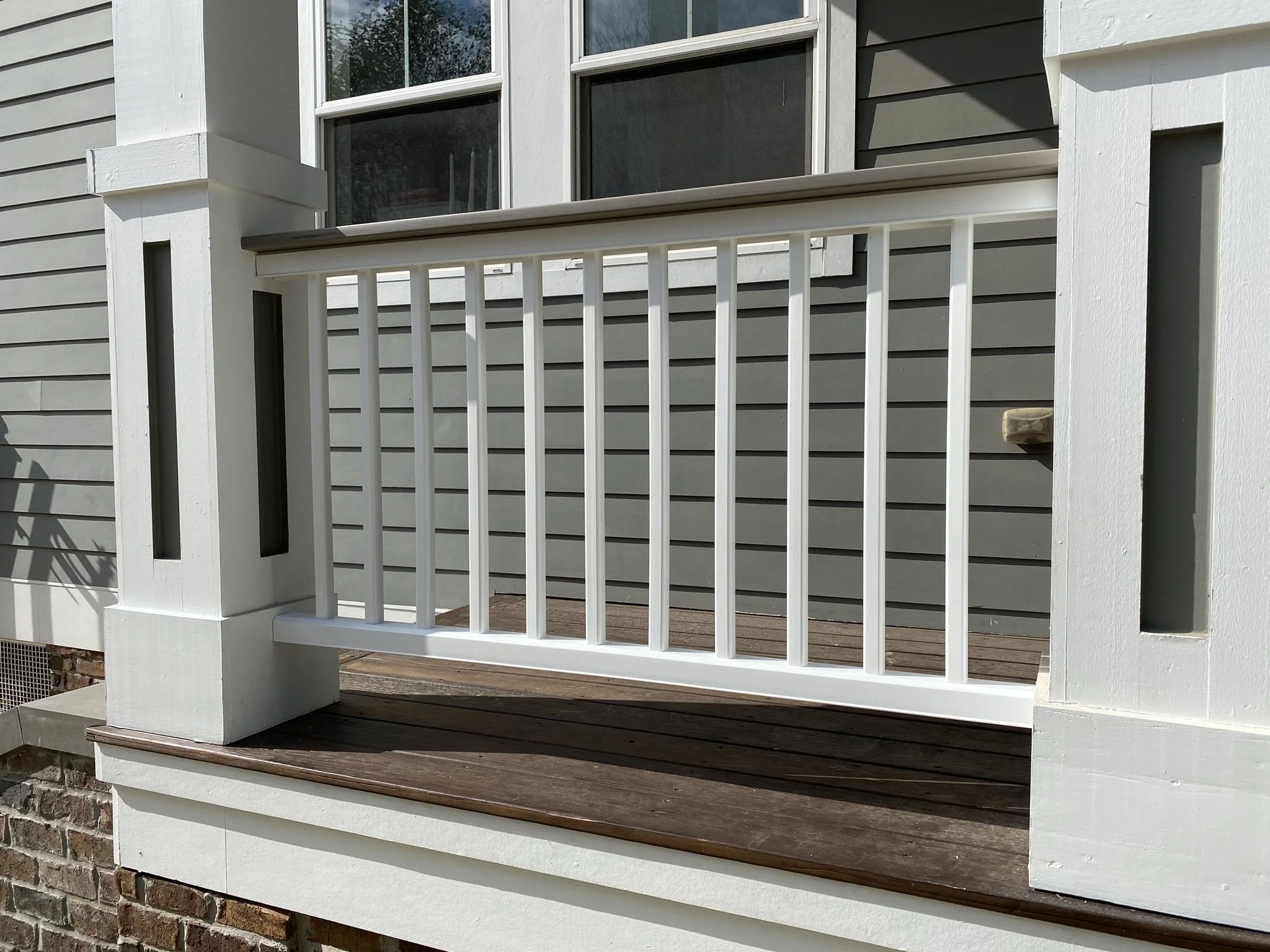 White porch railing with vertical slats, brown wood deck, and gray house siding in the background.