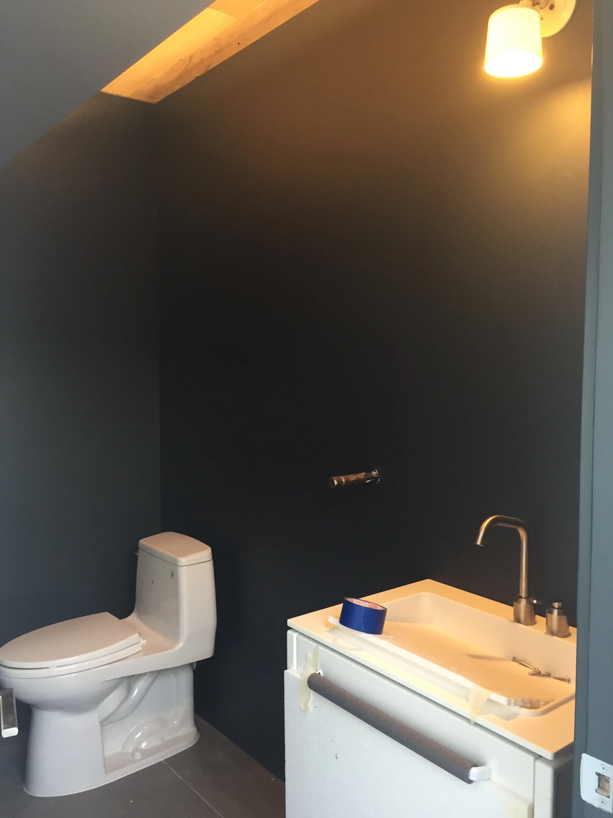 Bathroom under construction with a toilet and sink, dark walls, and overhead recessed lighting.