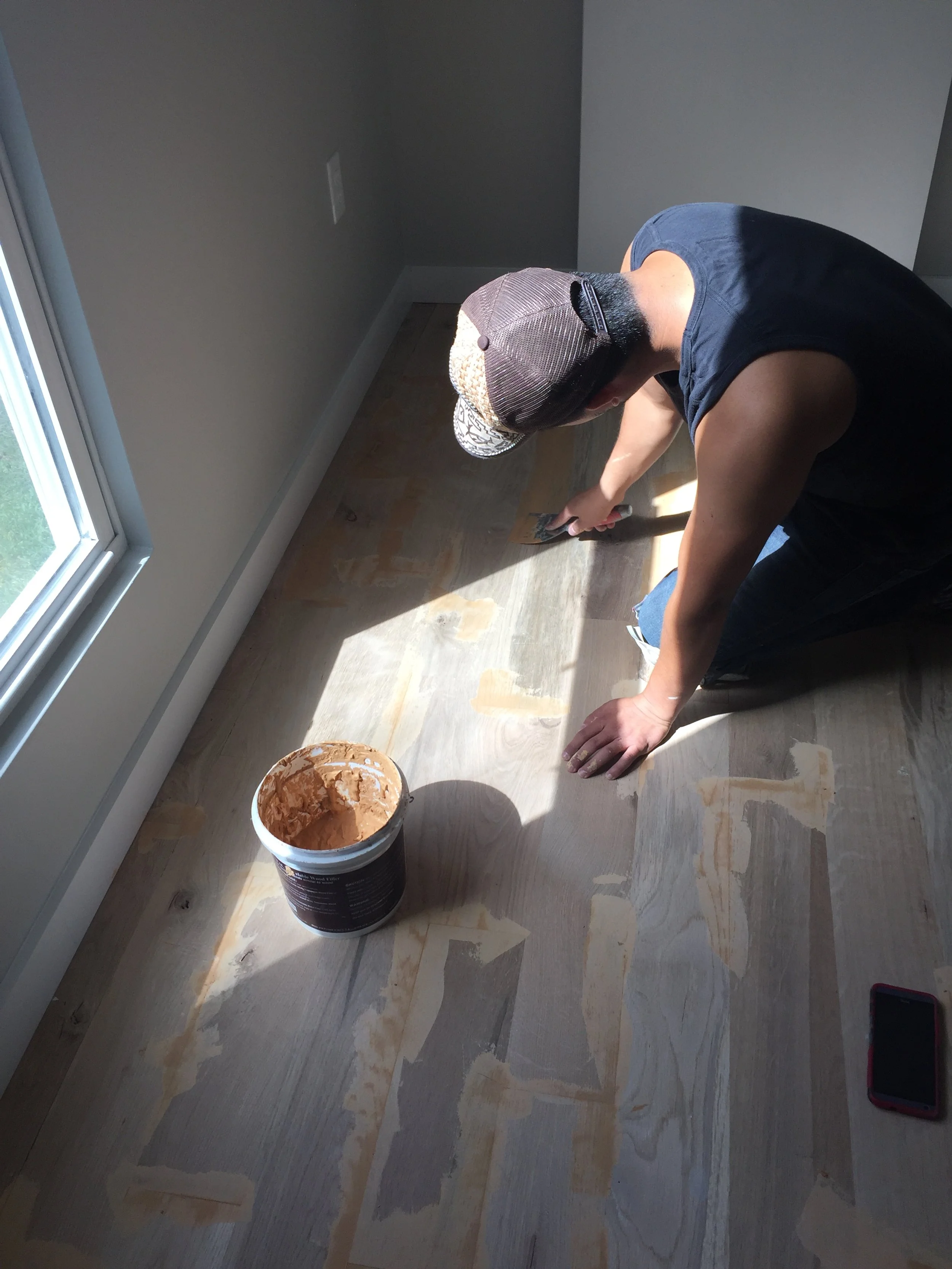 Person applying wood filler to a hardwood floor from an open container.