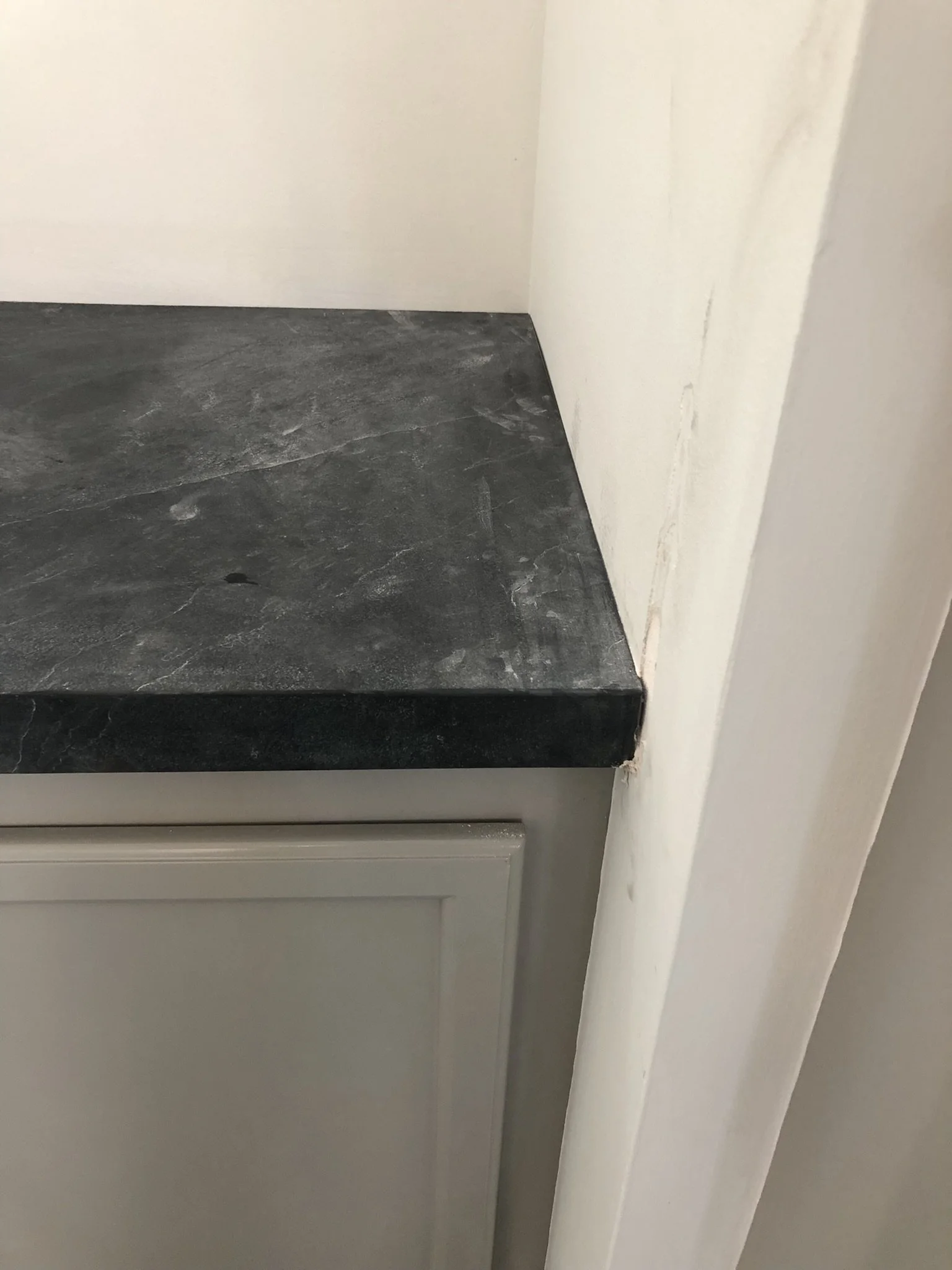 Close-up view of a dark stone countertop in a corner, adjacent to a light-colored cabinet and wall.
