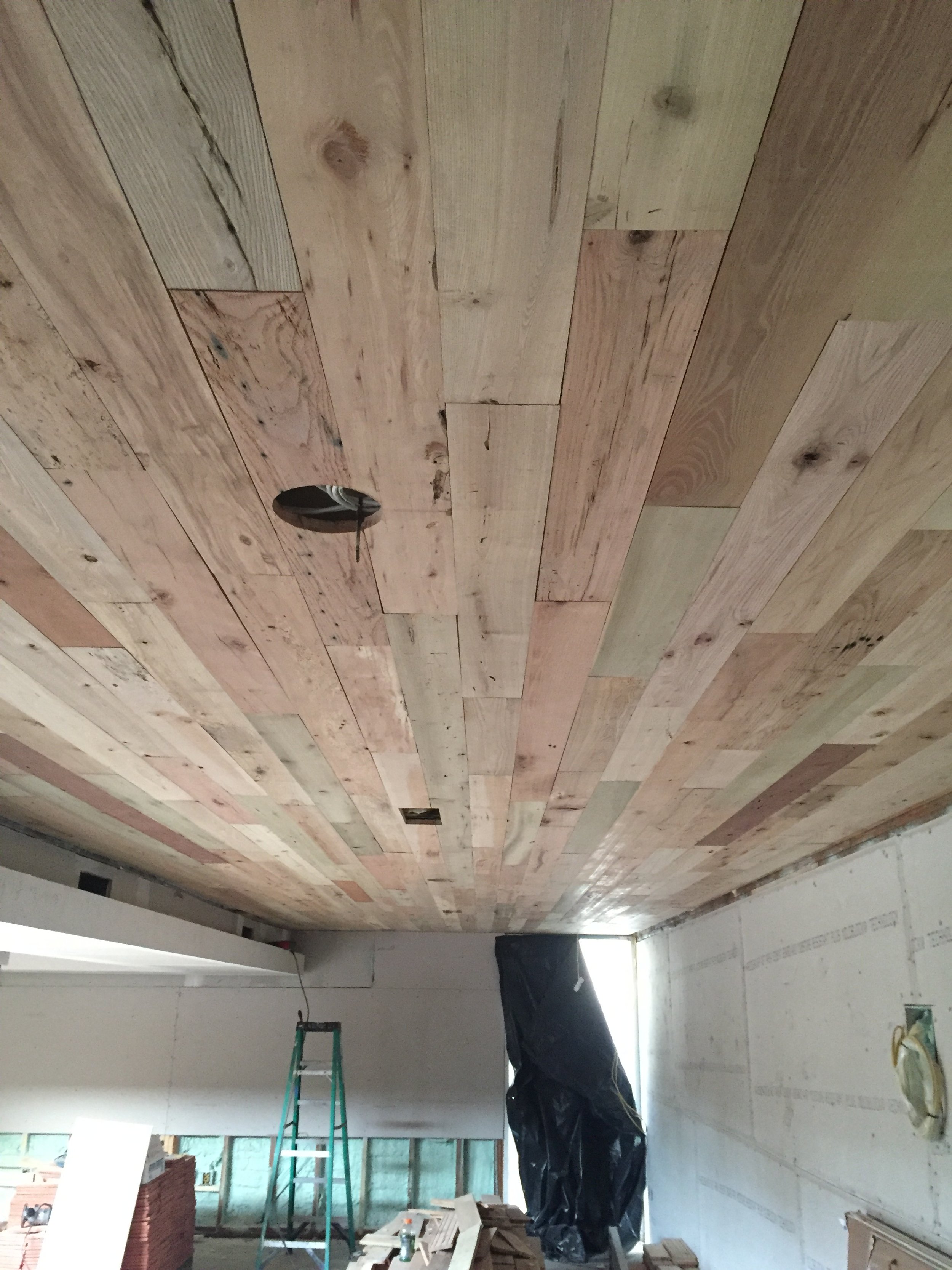 Wooden plank ceiling installation in a room under construction, with a step ladder and various building materials.