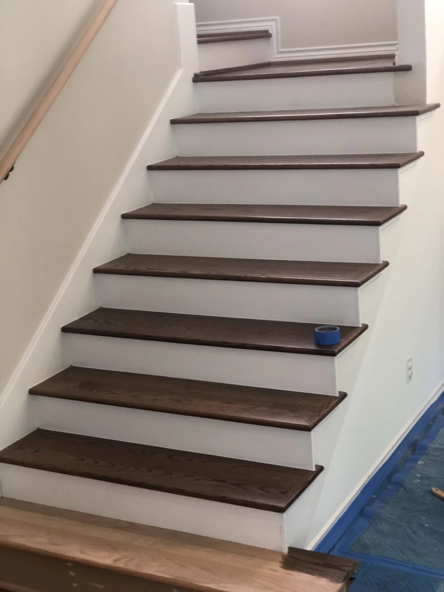 Indoor staircase with wooden steps and a roll of blue painter's tape on one step.