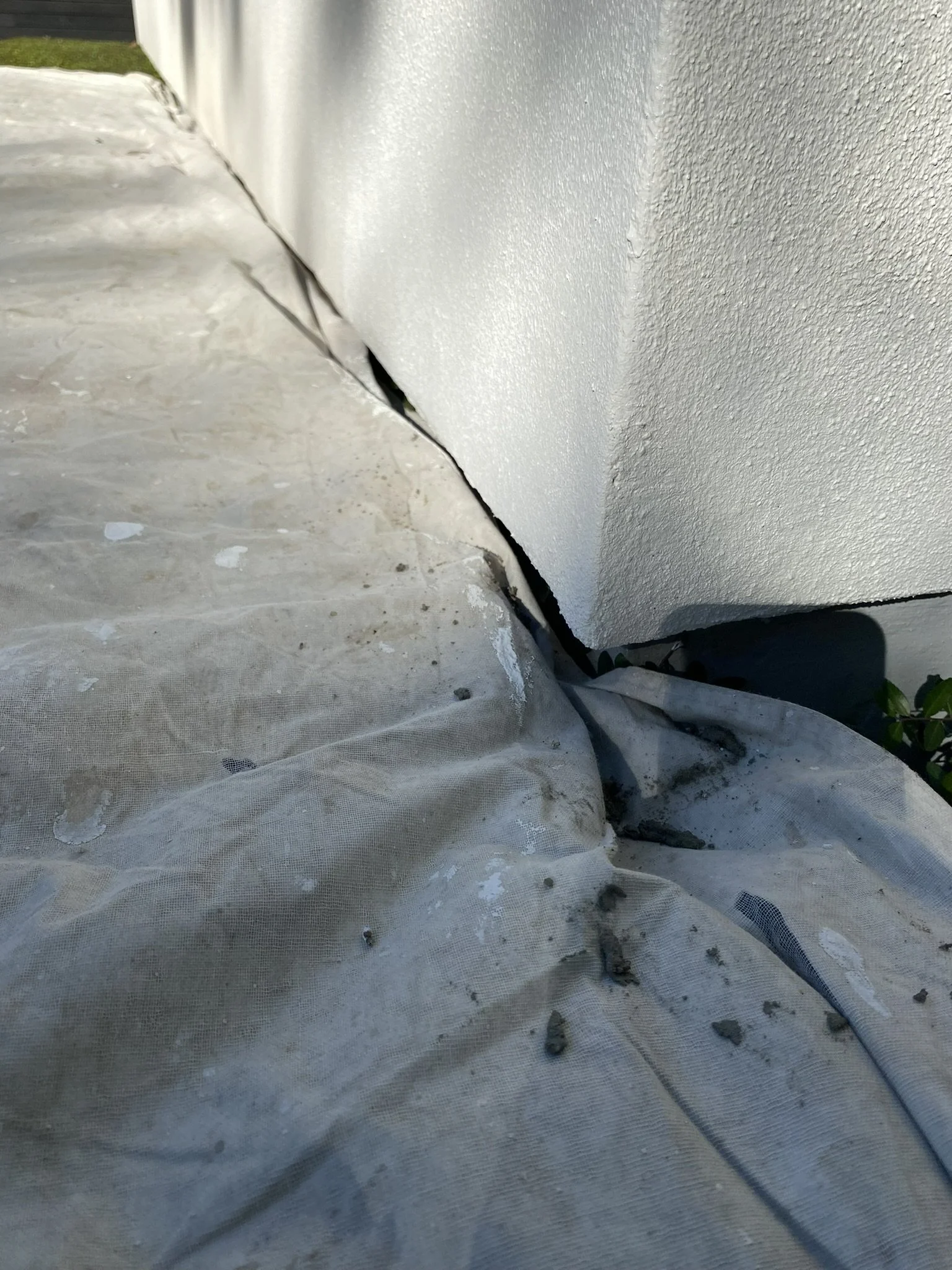 Crack in building wall at base, covered with tarp.
