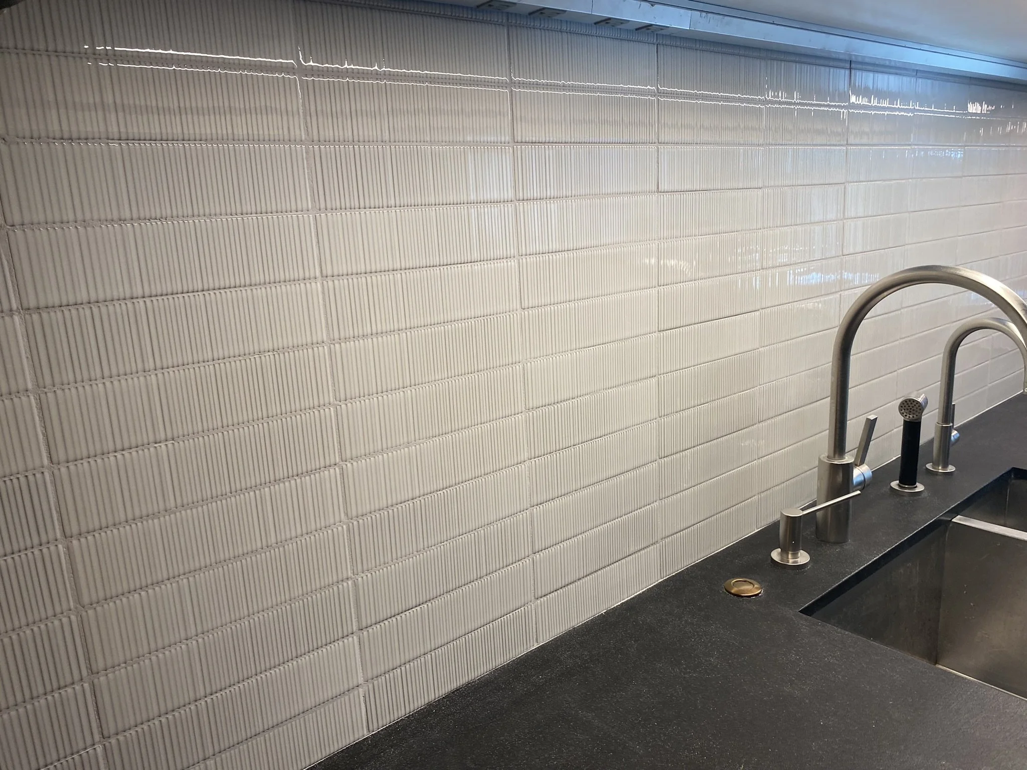A kitchen sink with a modern faucet, placed on a dark countertop and backed by a tiled wall with vertical lines.