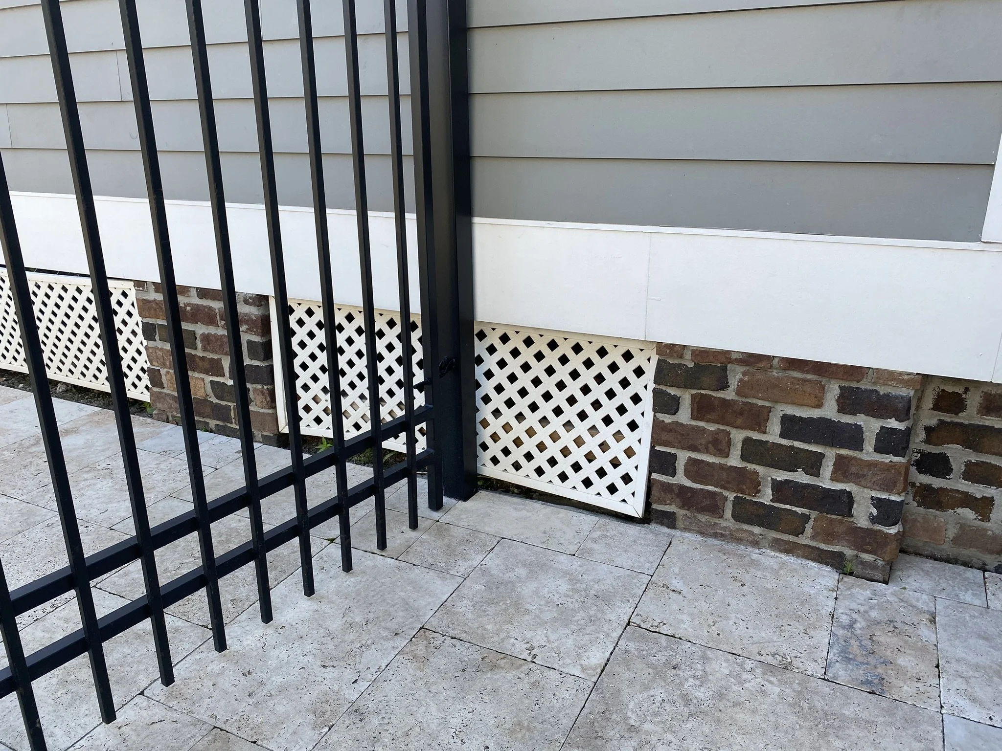 Black metal fence in front of a textured wall with brick and lattice design.