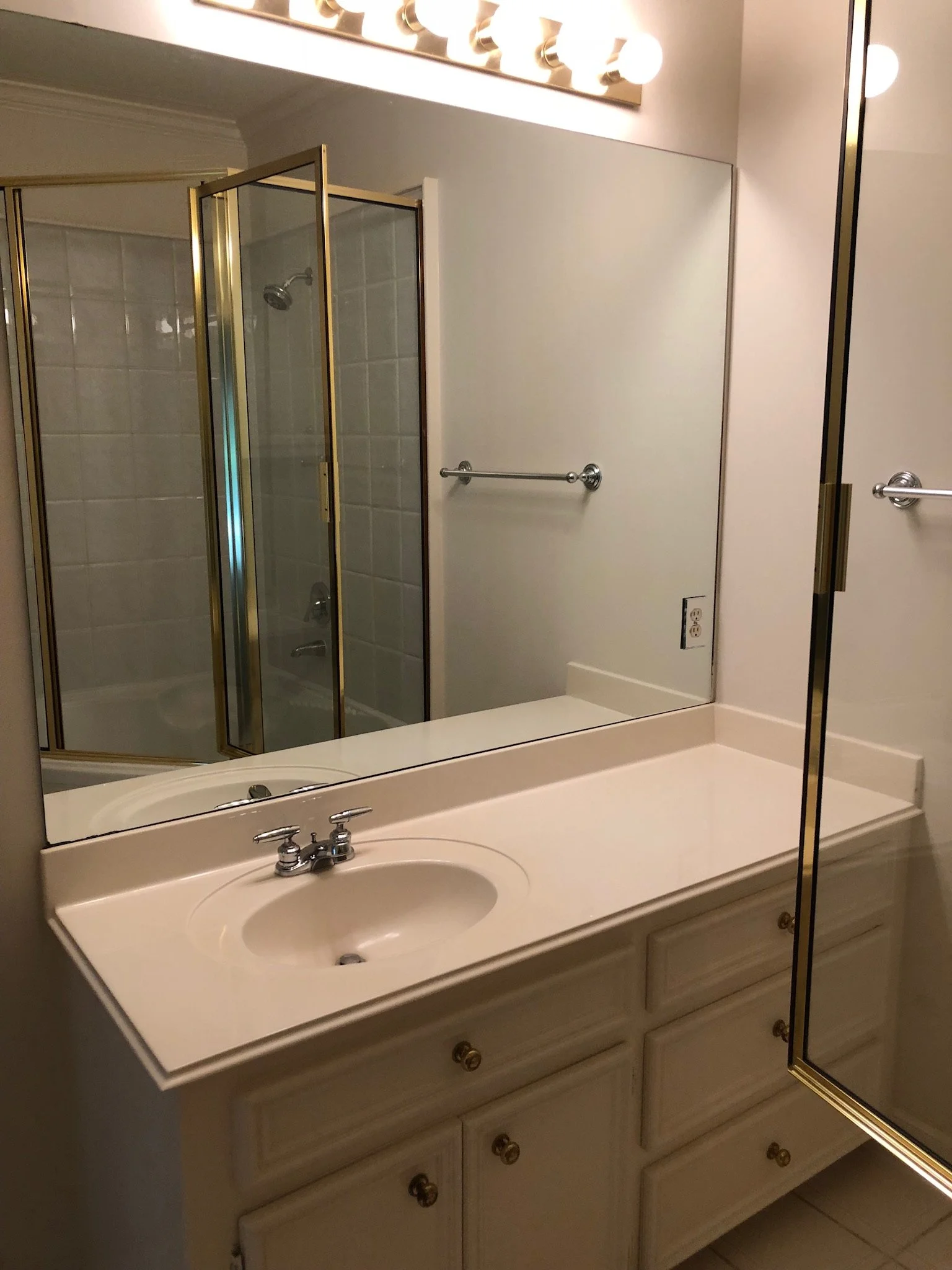 Bathroom with a vanity, sink, large mirror, and a gold-trimmed glass shower.