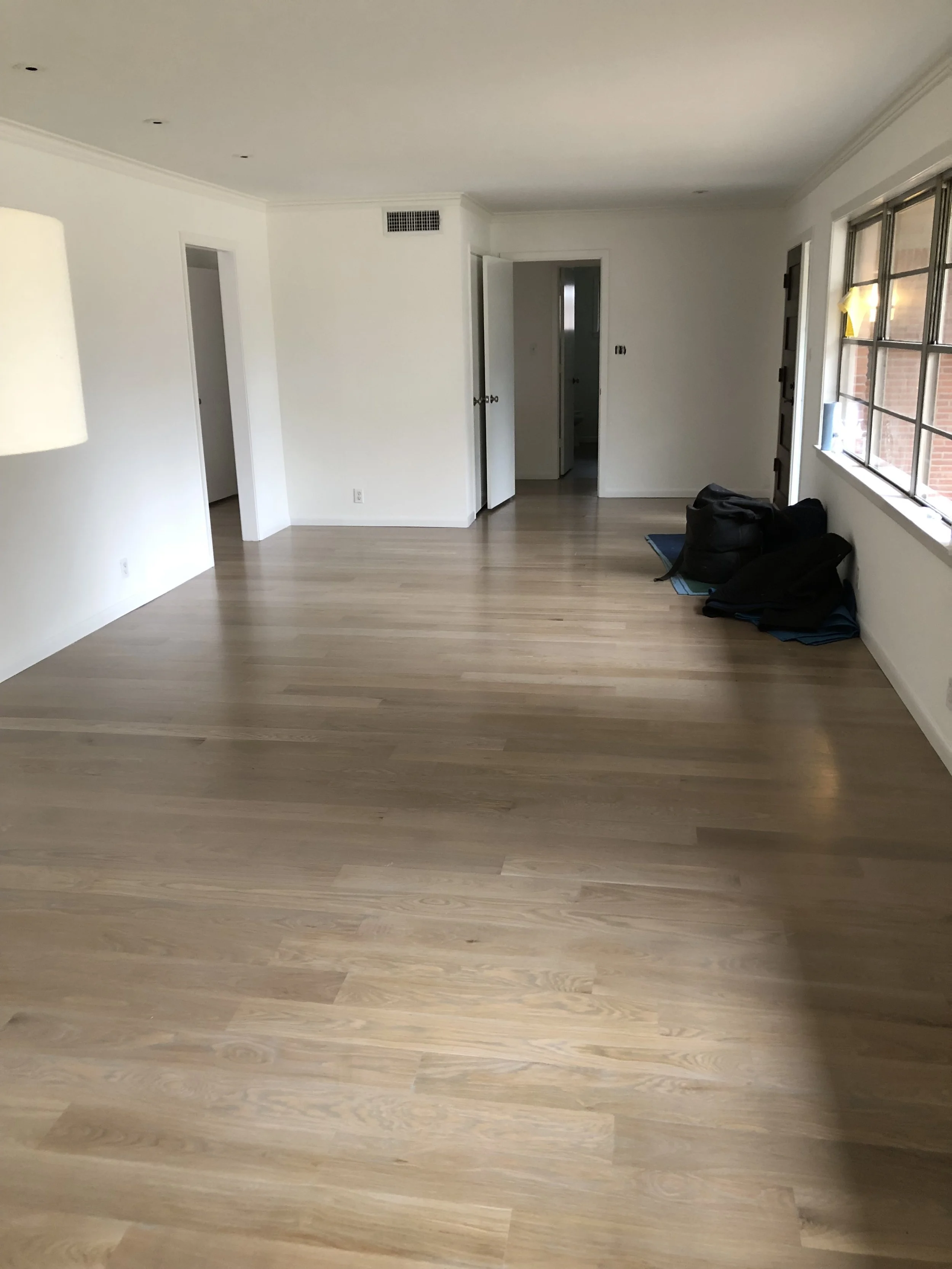 Empty room with light wooden flooring, white walls, and multiple doors. There are a few bean bags near the window on the right.