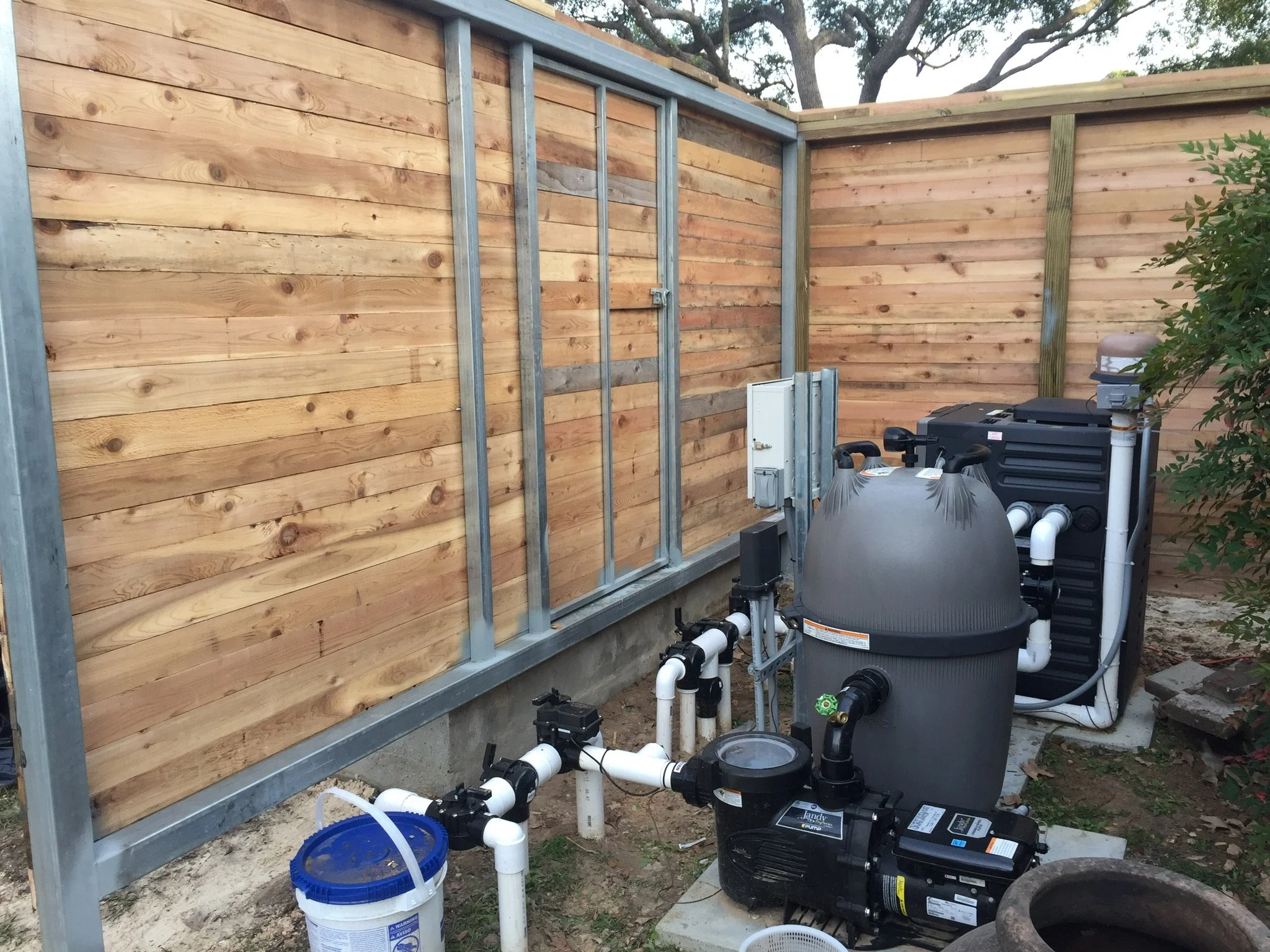 Outdoor swimming pool pump and filter system beside a wooden fence