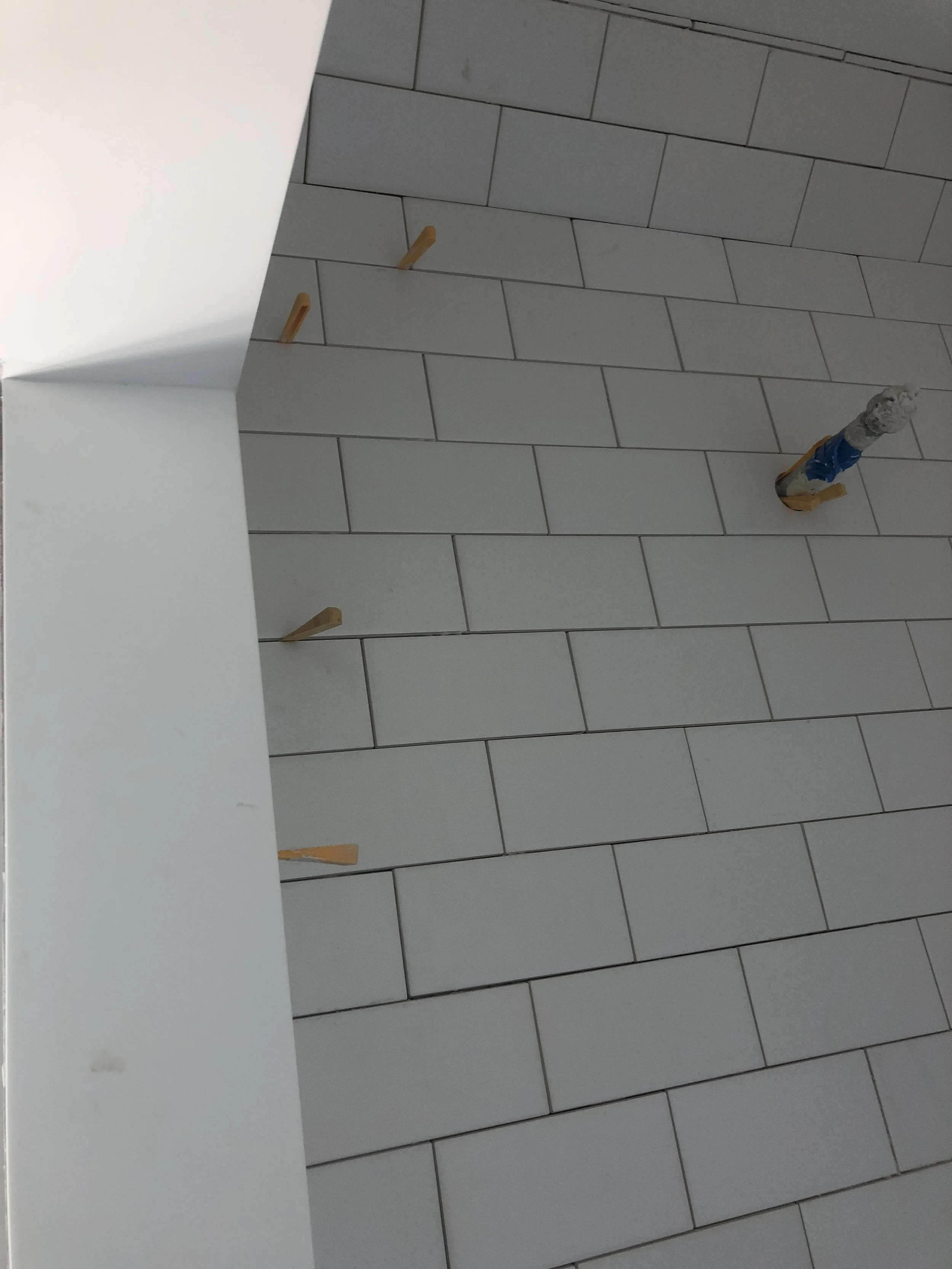 Tiled wall with white rectangular tiles and wooden spacers between them, partially finished with a taped pipe section.