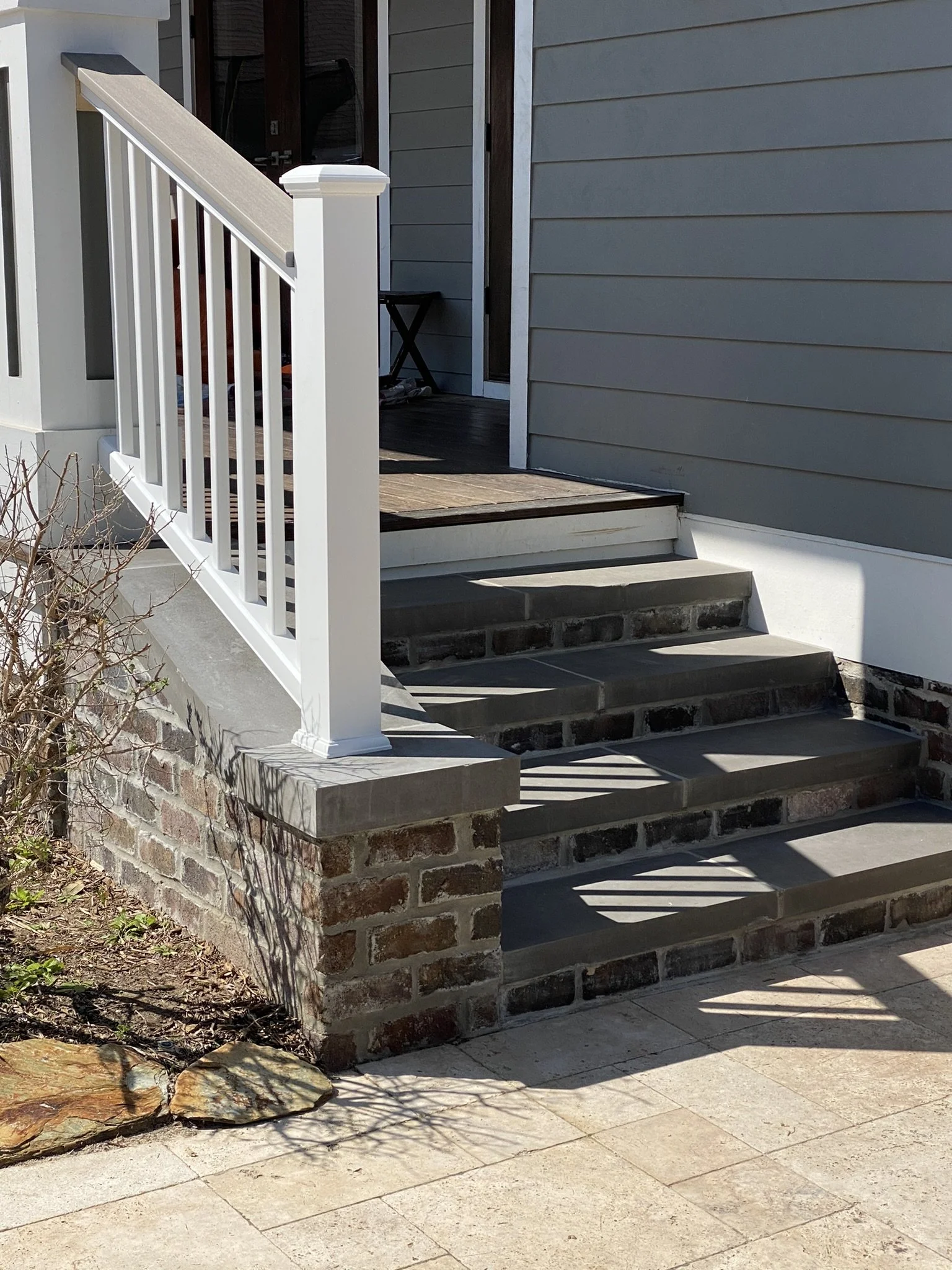 Outdoor brick steps with a white railing leading to a porch of a gray house.