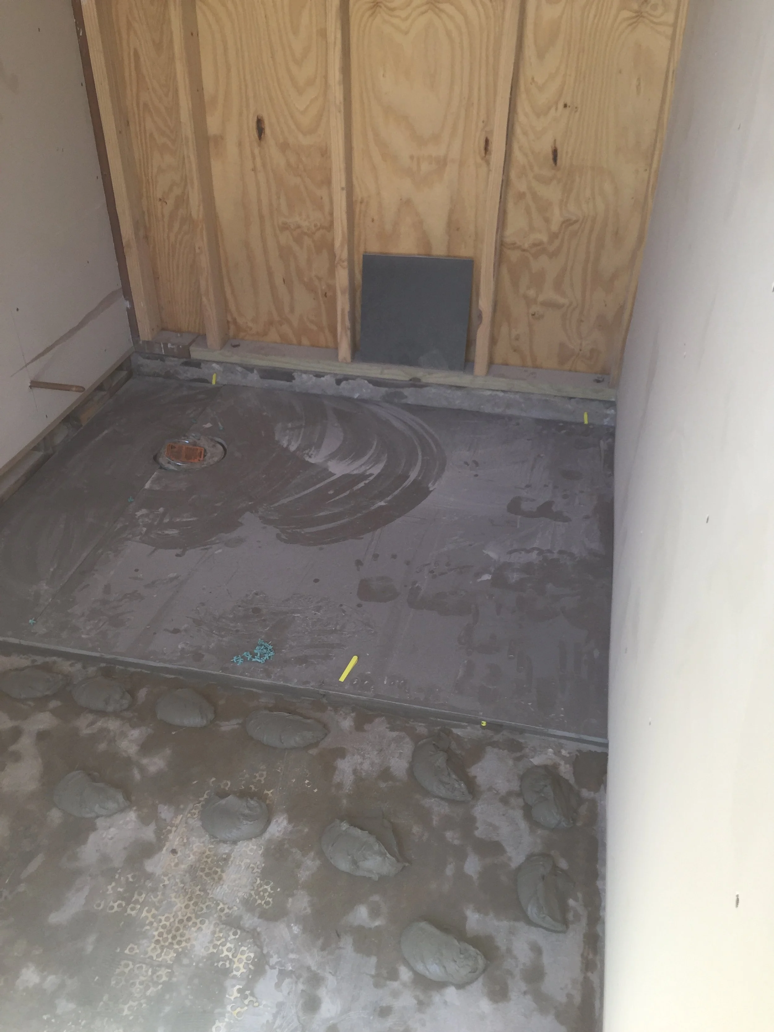 Unfinished bathroom with plywood walls, shower area under construction, and cement applied on floor.