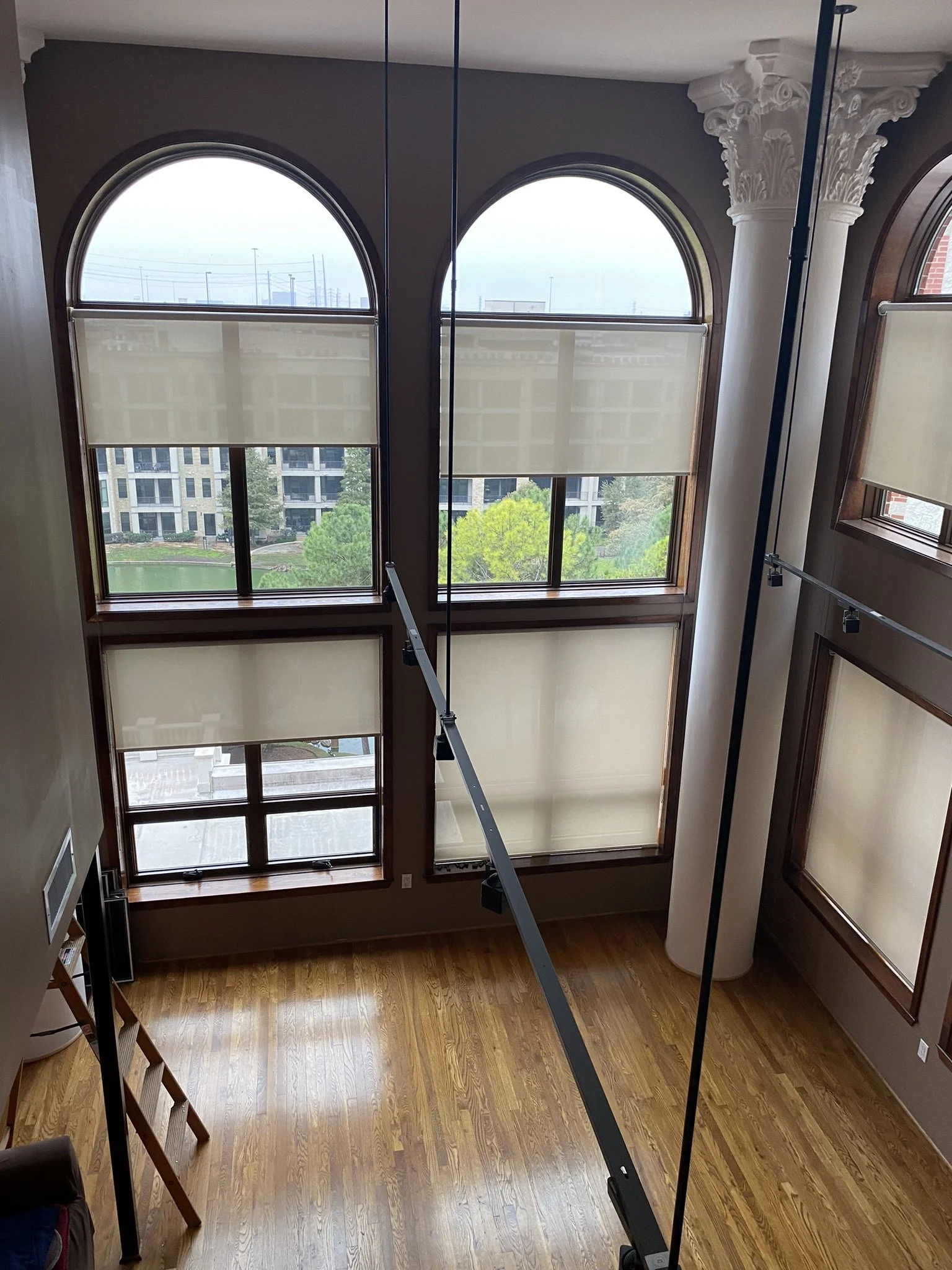 High-ceilinged room with large arched windows, wood flooring, and white blinds.