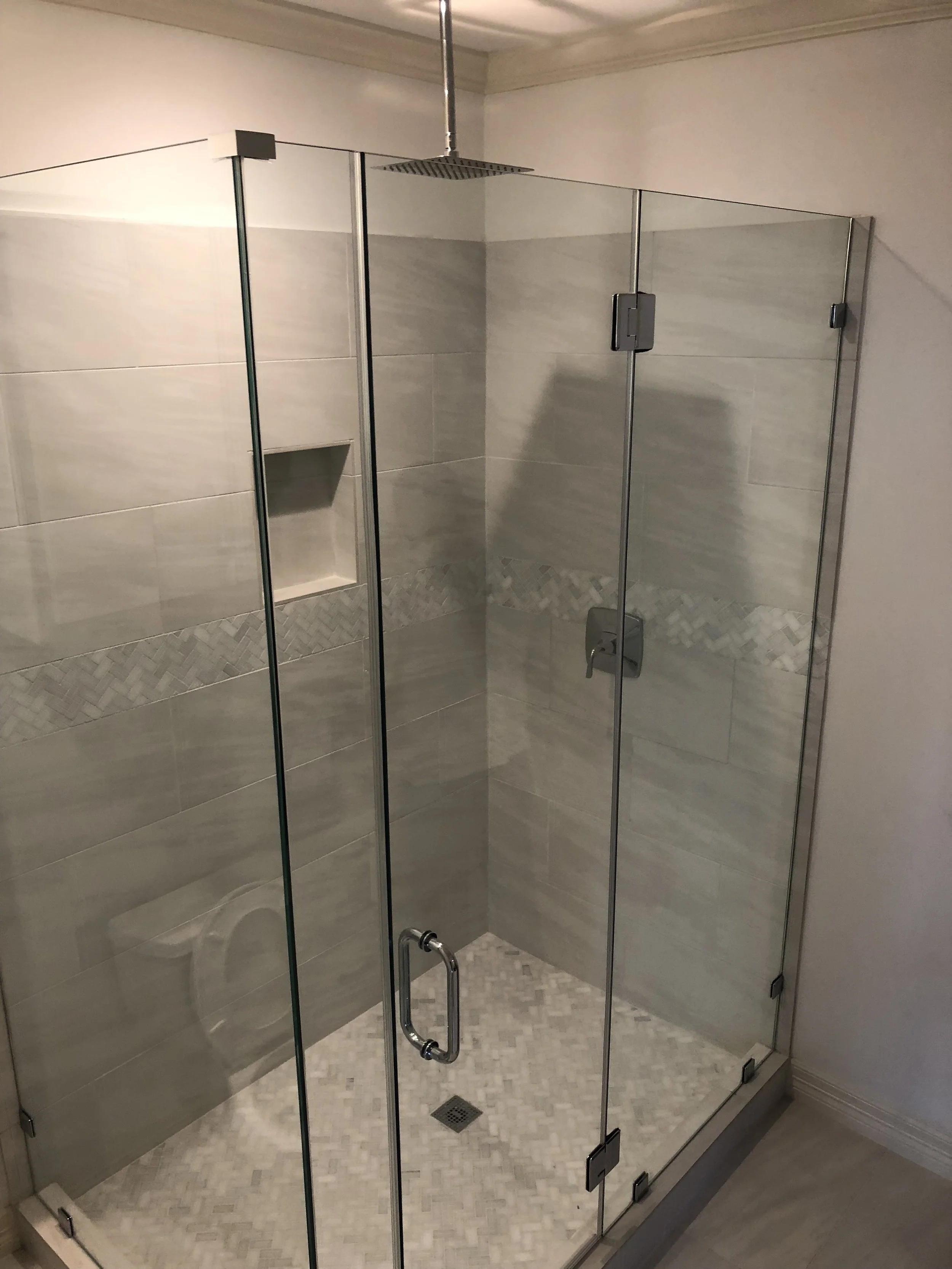 Modern glass shower enclosure with rainfall showerhead and decorative tile design.