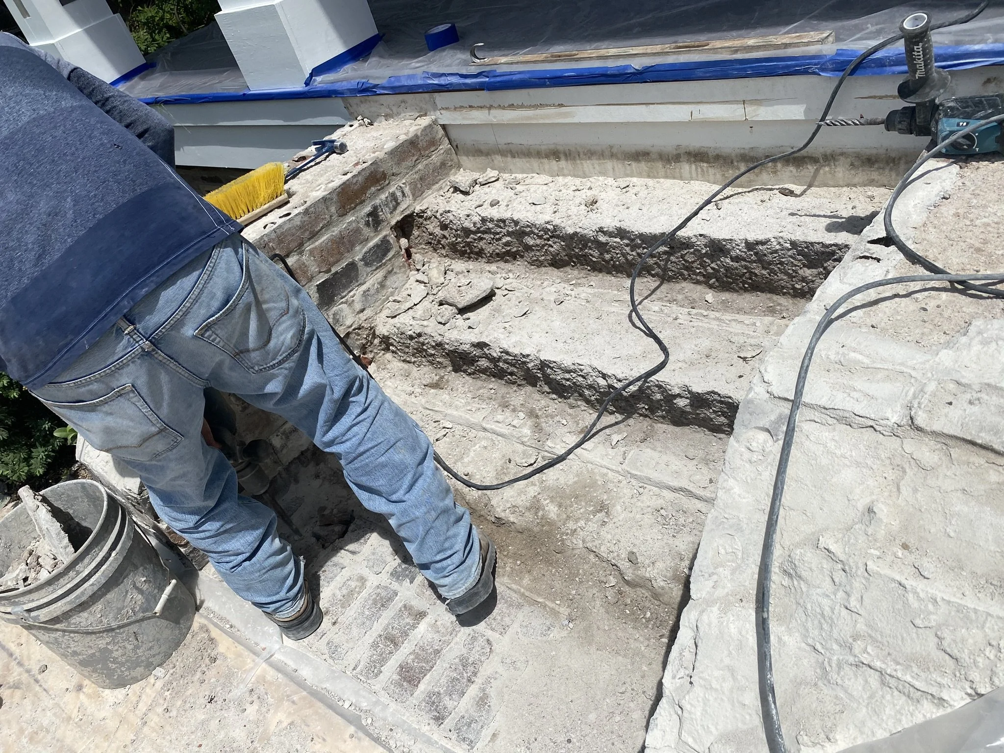 J. Luis Construction Inc worker is working on damaged brick steps with construction tools and materials nearby.