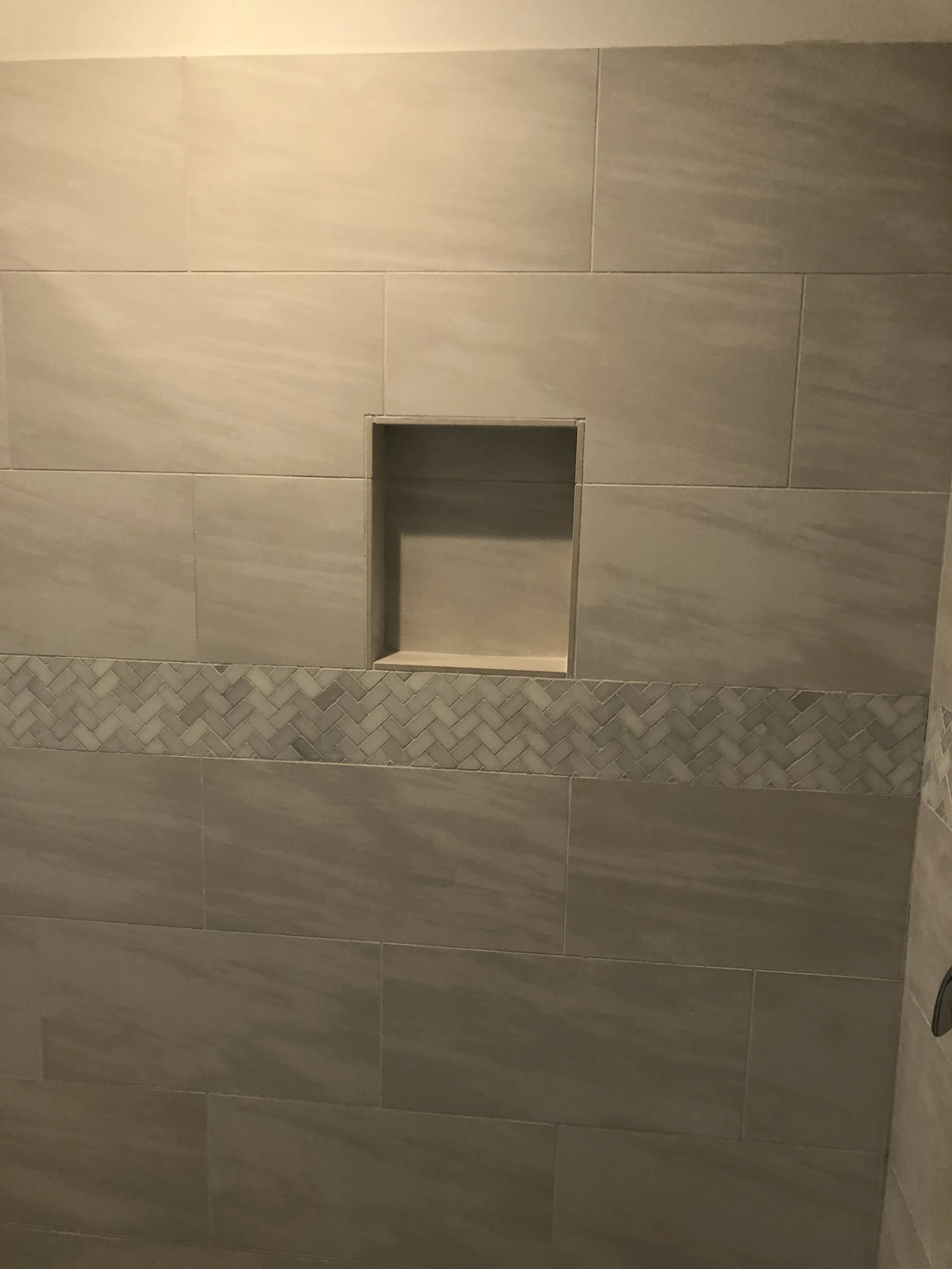 Bathroom wall with beige tiles and a small recessed shelf.