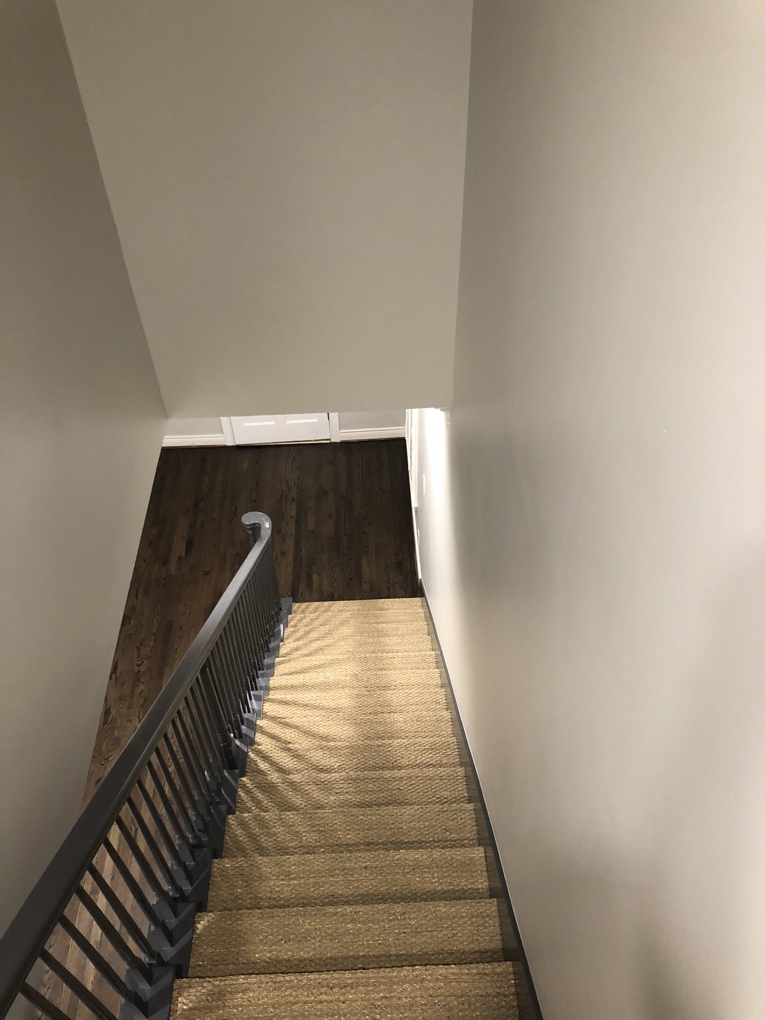 View looking down a staircase with wooden steps and a railing, leading to a hardwood floor hallway.