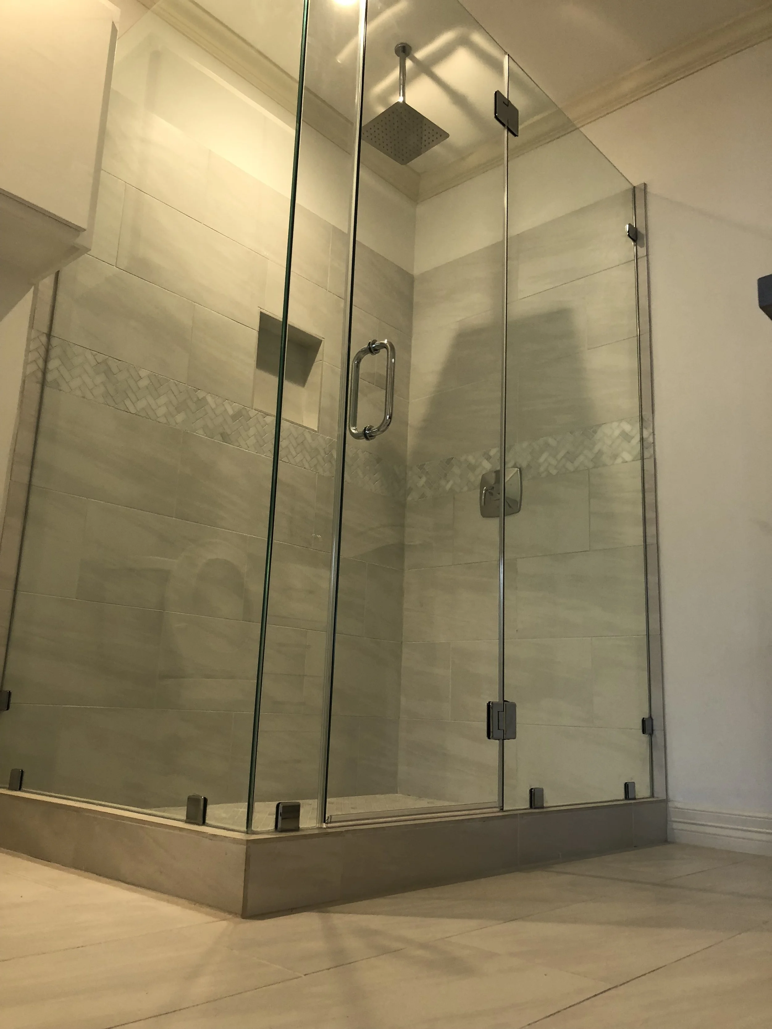 Modern glass shower with beige tile walls and a rainfall showerhead.