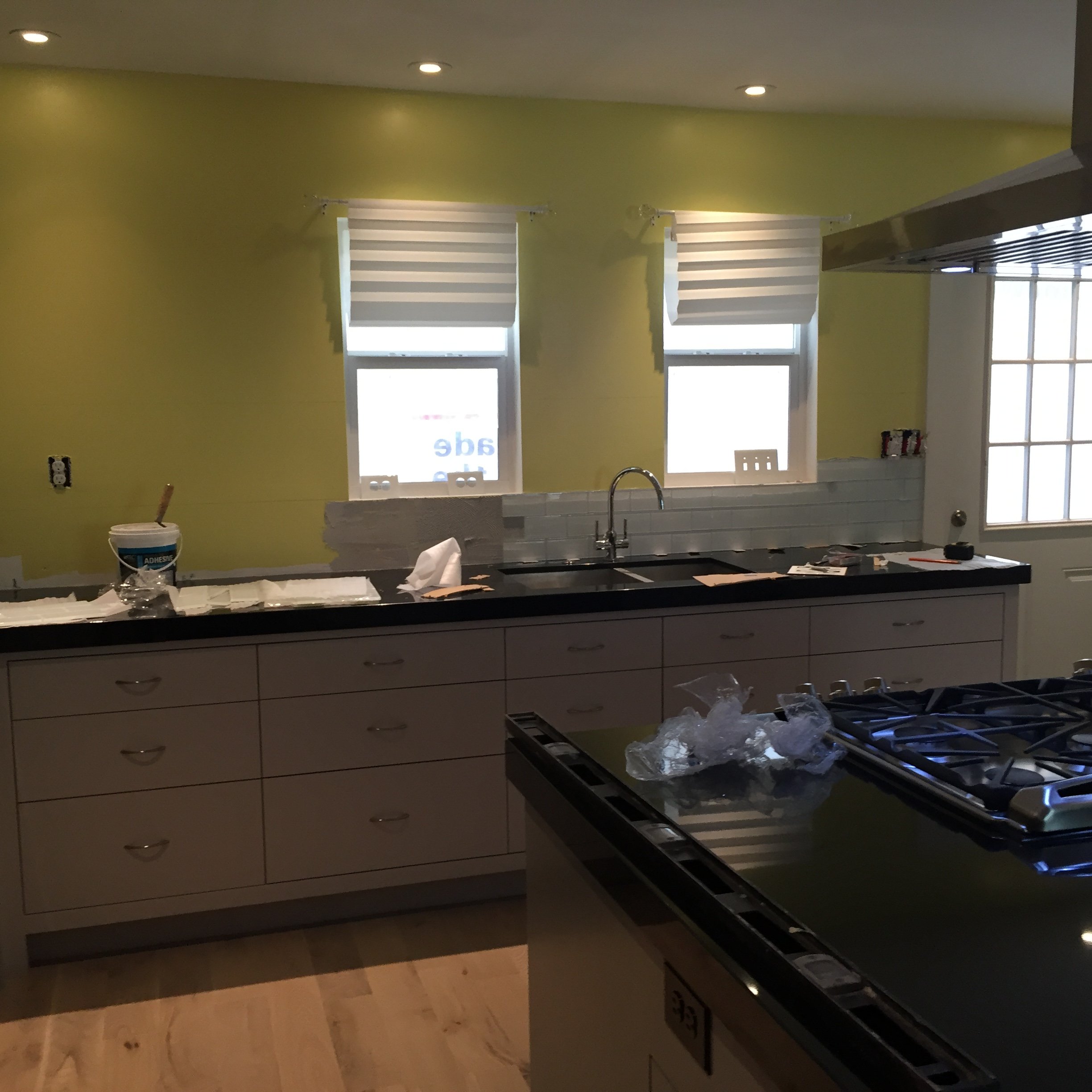 Modern kitchen under renovation, featuring a yellow wall, white cabinetry, black countertops, a sink, a gas stove, and construction materials.