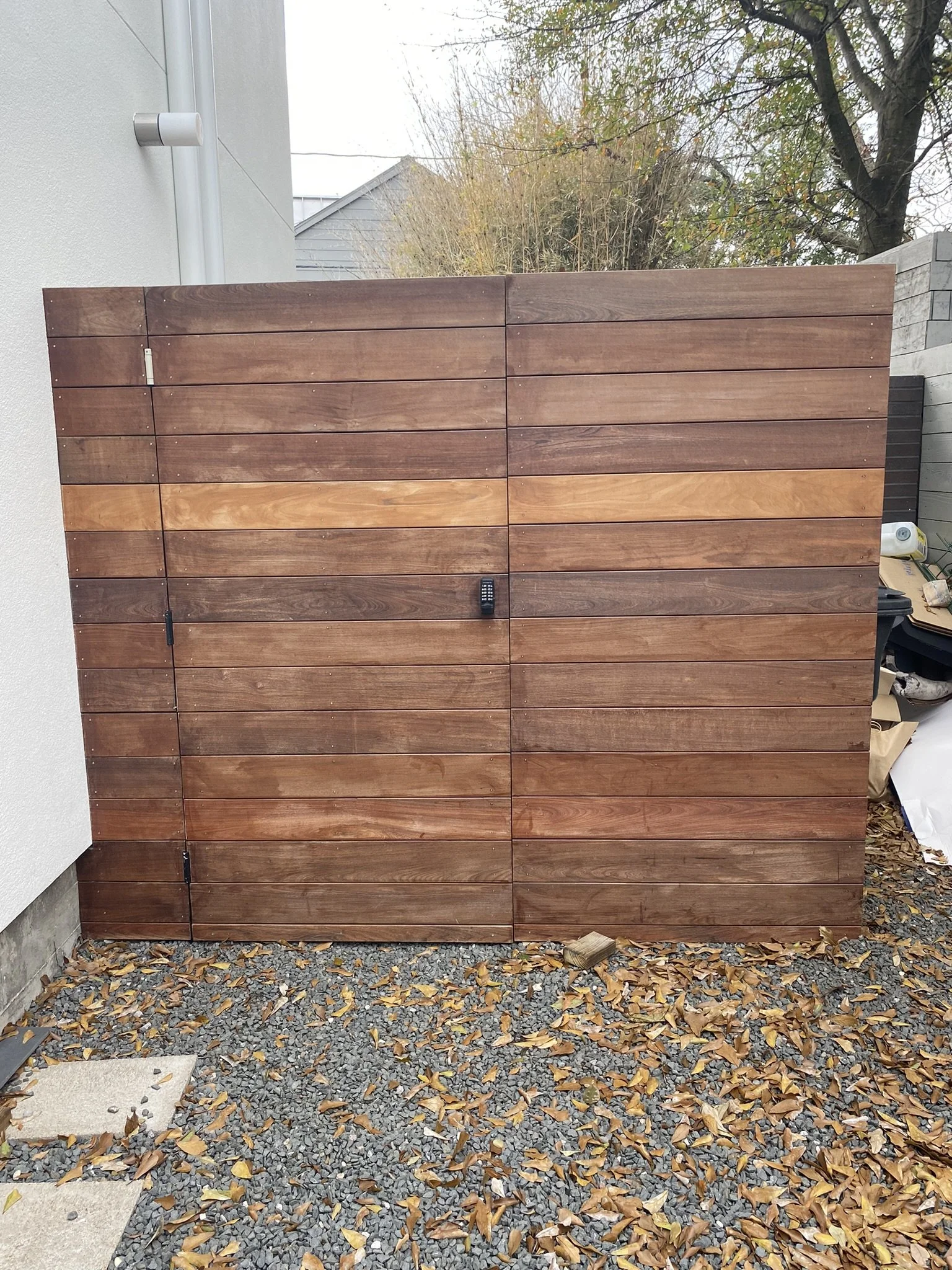 Wooden fence gate with lock and pebbled ground covered with leaves