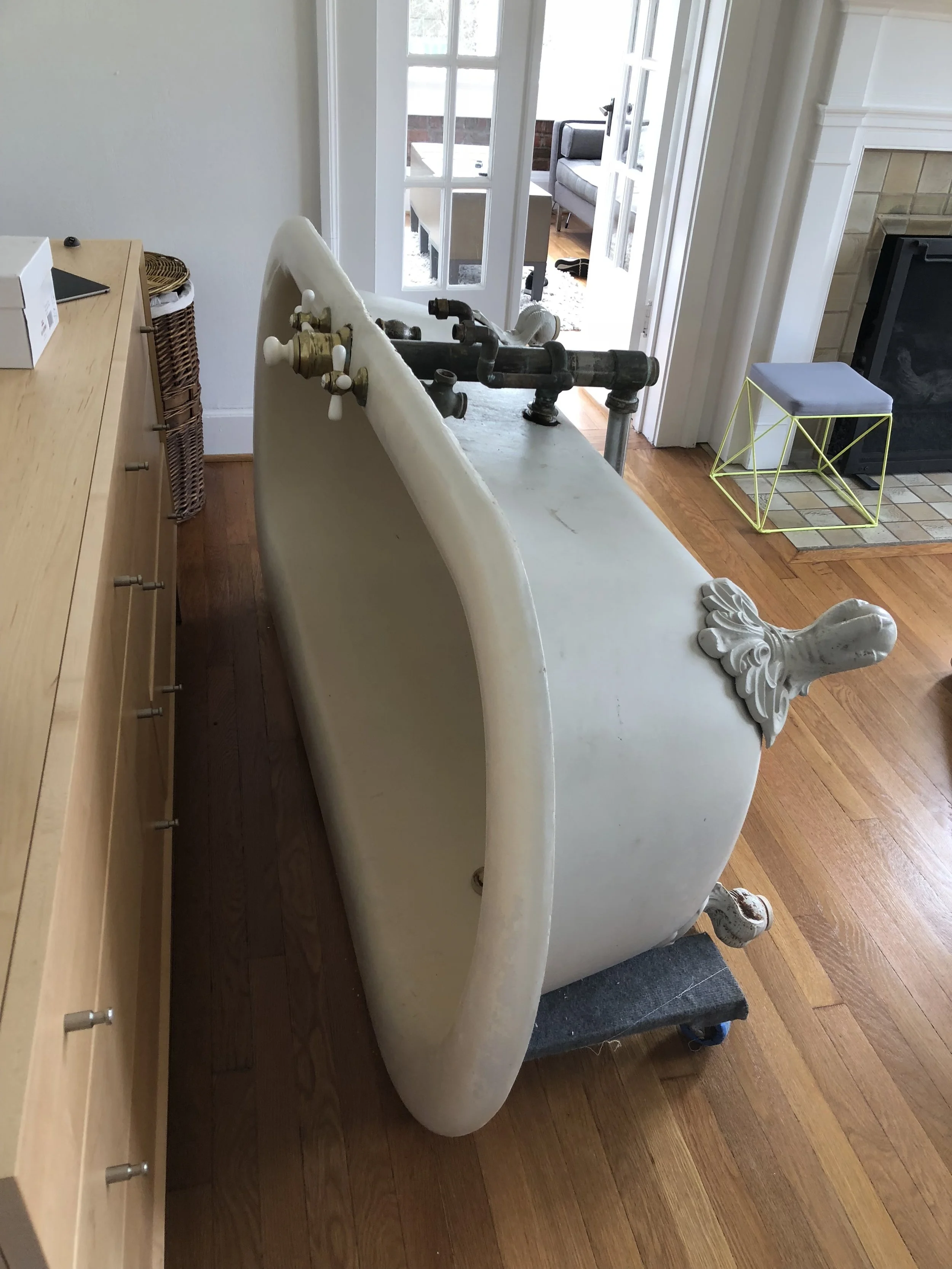 Antique clawfoot bathtub on a dolly in a living room with hardwood floors, near a fireplace and furniture.
