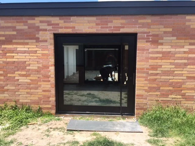A brick wall with a black sliding glass door and grass in front.