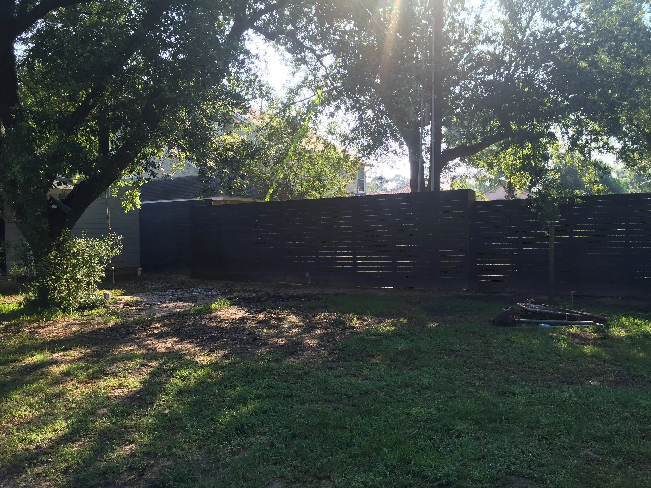 Backyard with wooden fence, trees, and grass lawn in sunlight.